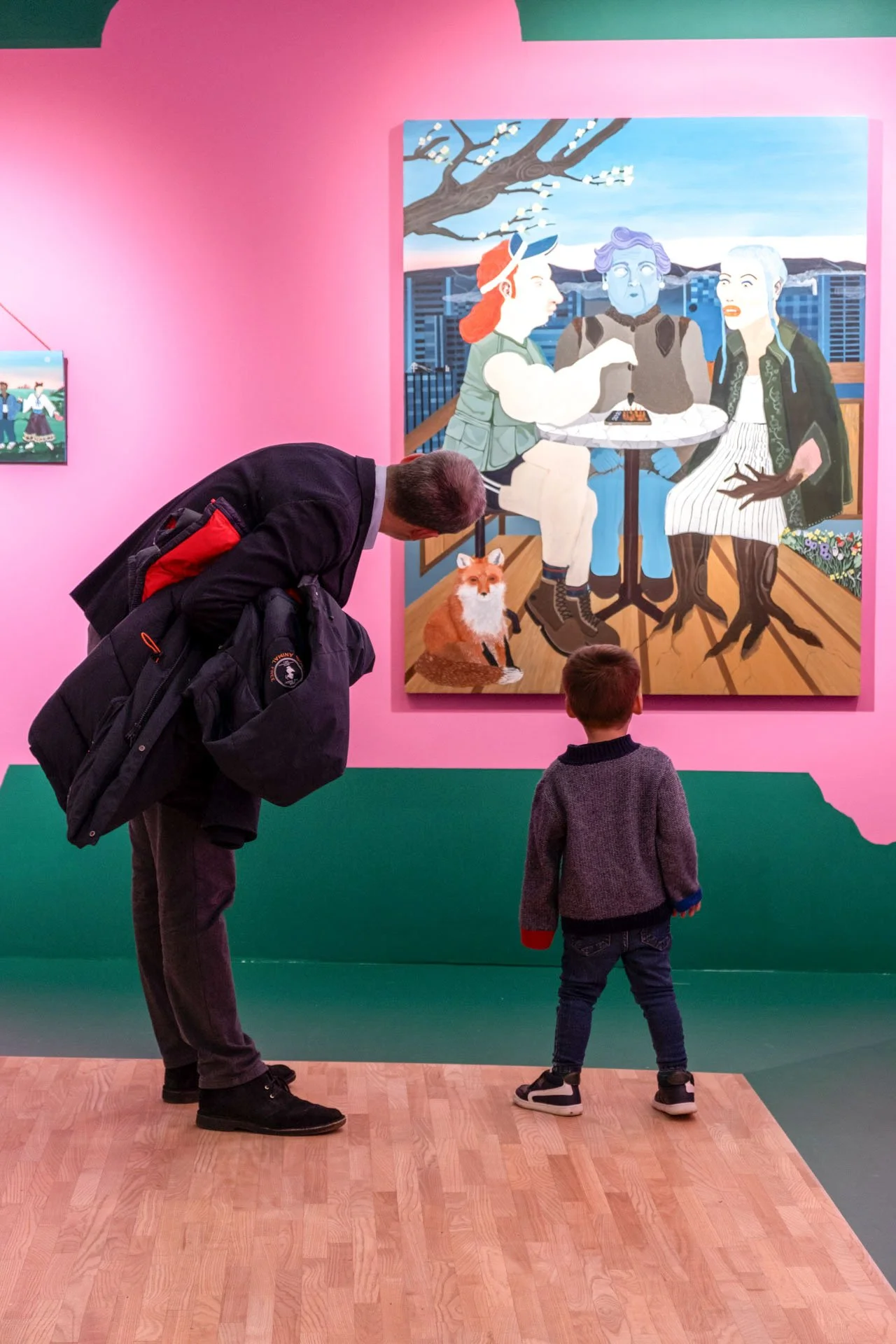 Un homme, un enfant et un chien regardent une peinture dans une galerie d'art. La peinture représente trois personnes assises à une table, avec un arbre en arrière-plan.