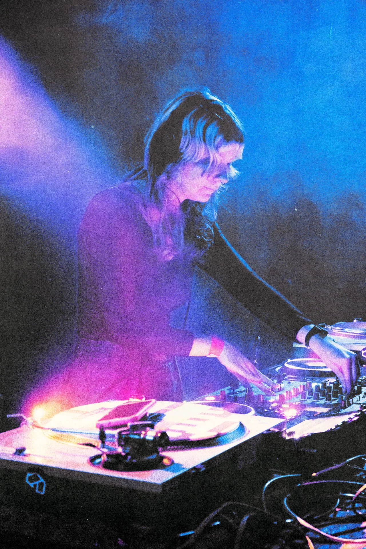 Une DJ mixant de la musique dans un environnement sombre avec des lumières violettes et bleues.