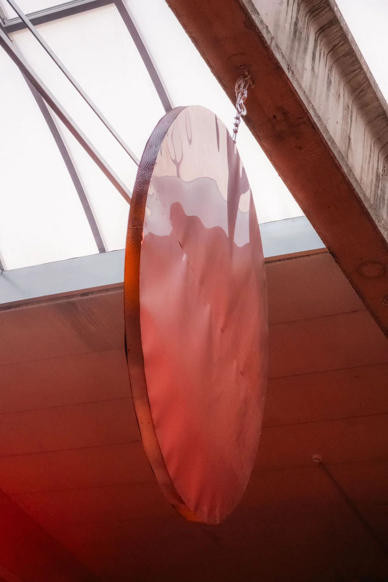 Une planche de surf suspendue par une chaîne au plafond, vue de dessous, dans un espace intérieur avec un plafond en verre.