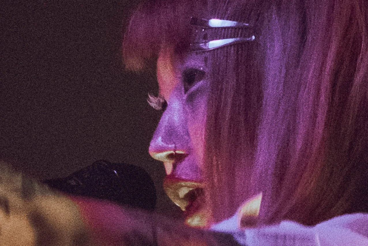 Une personne avec des lunettes, exprimant une émotion intense dans un environnement sombre avec une lumière violette.