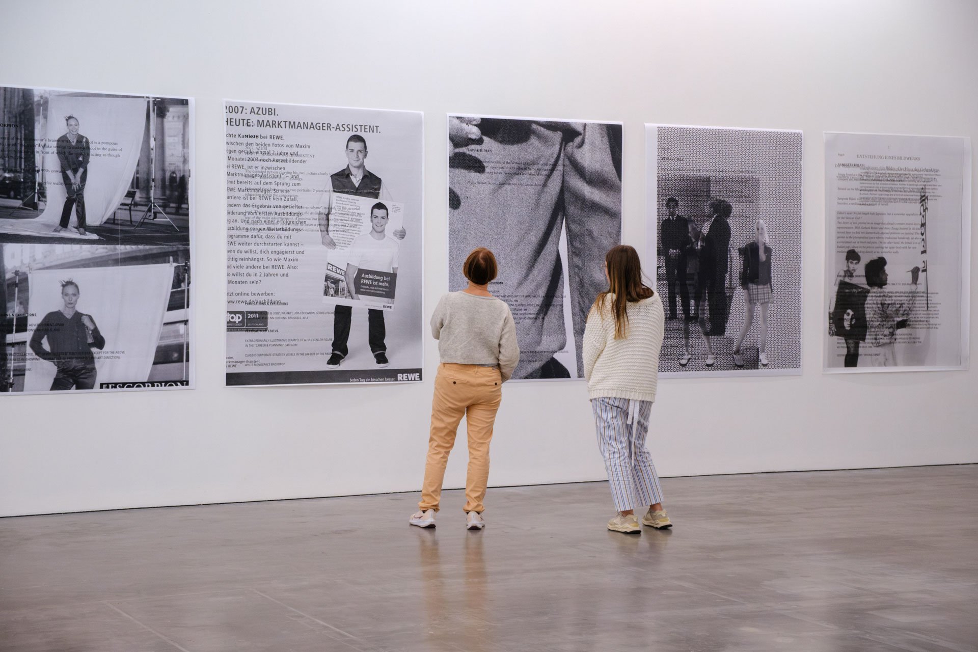 Deux femmes regardent une série d'affiches en noir et blanc dans une galerie d'art.