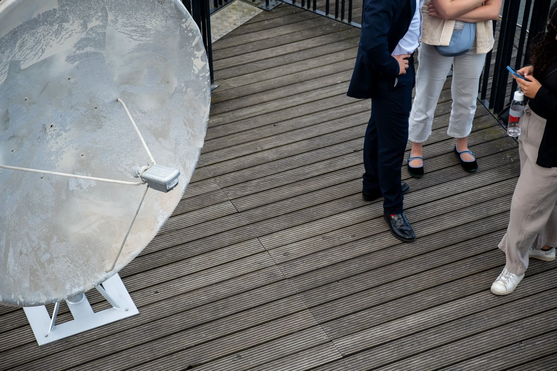 Groupe de personnes debout sur une terrasse en bois, près d'une grande antenne parabole.