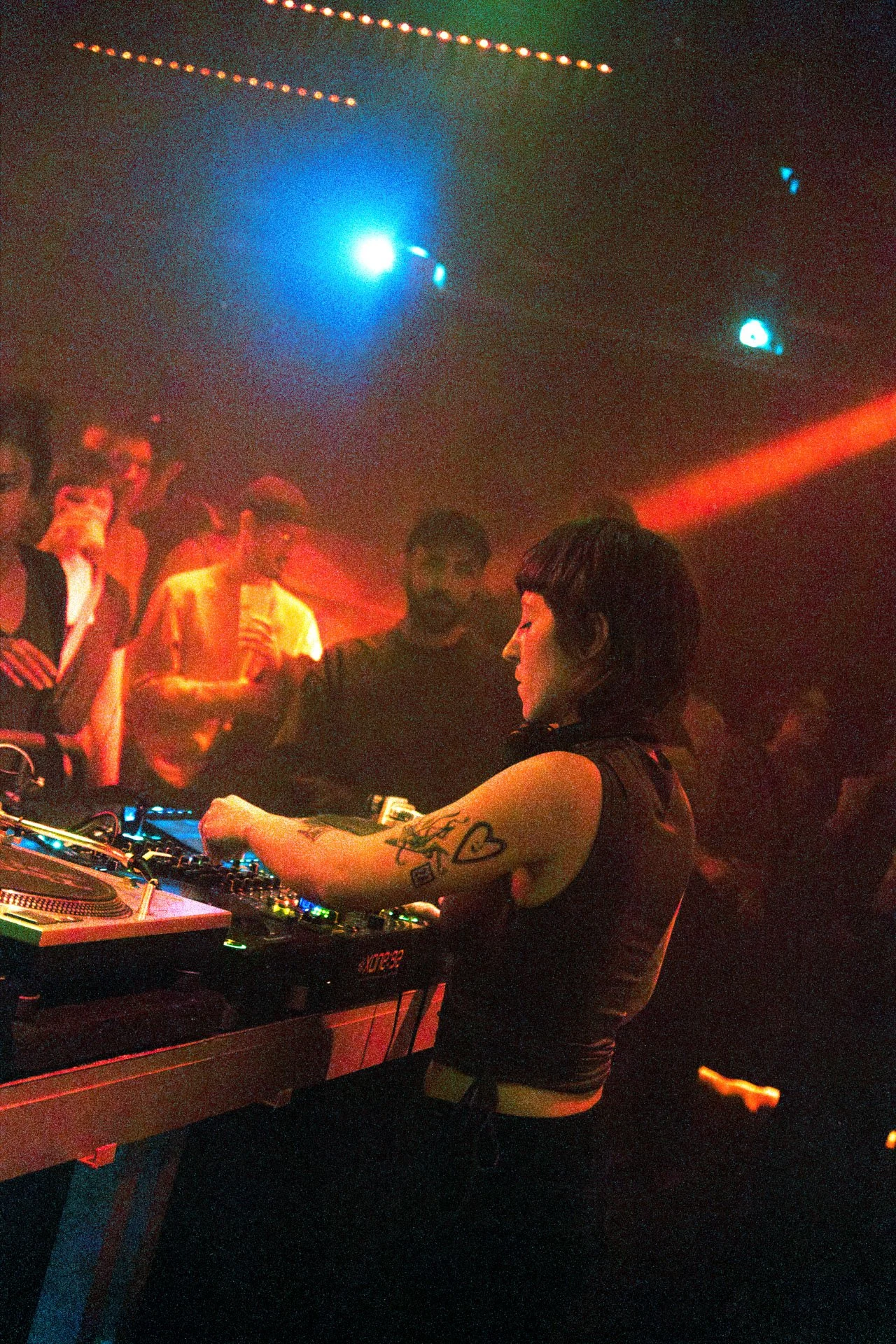 Une DJ féminine joue de la musique dans une soirée en nightclub avec des personnes qui dansent et la lumière colorée