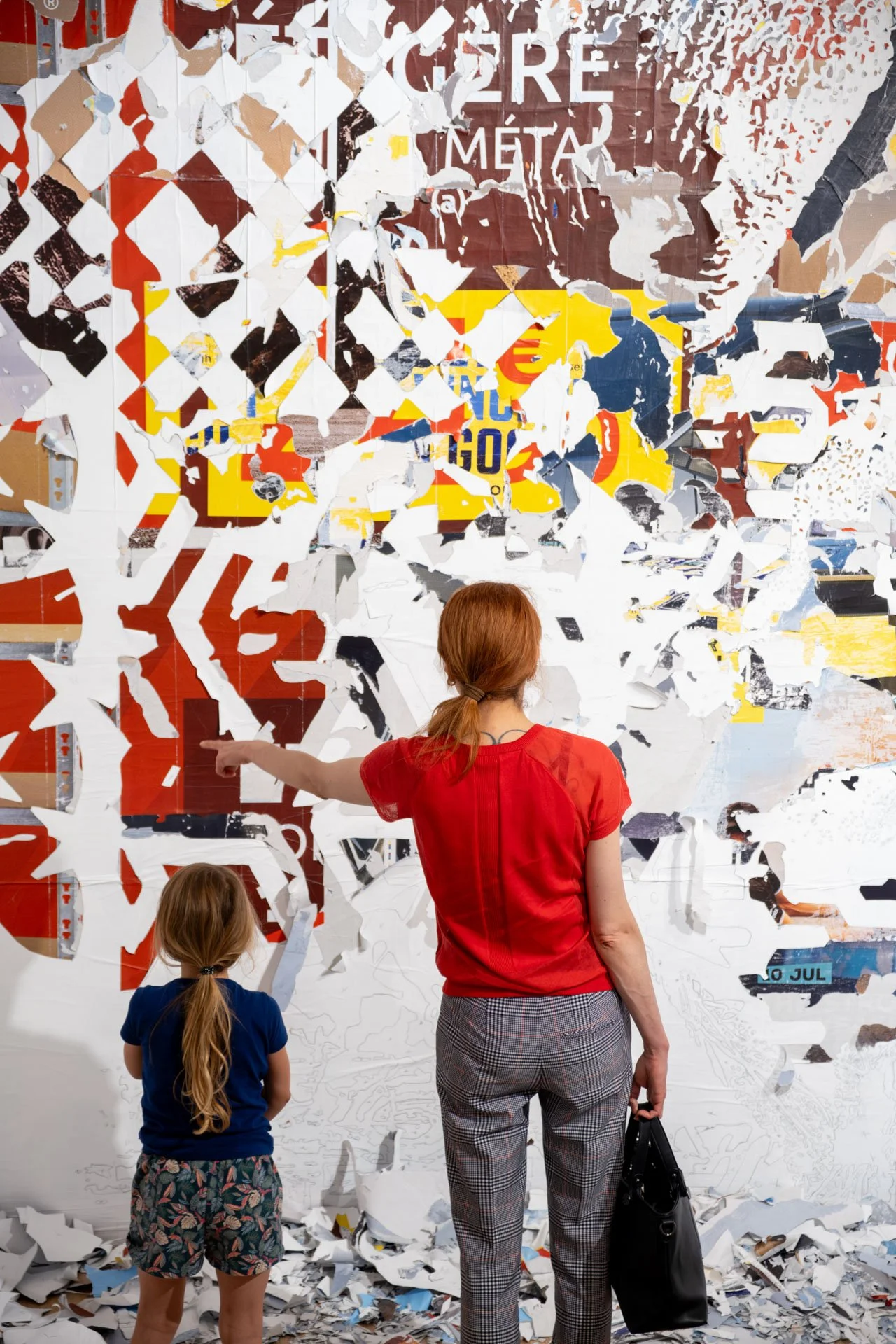 Une mère avec deux enfants, une fille et une fille, qui regardent un mur en mosaïque partiellement déchiré dans un espace d'exposition.