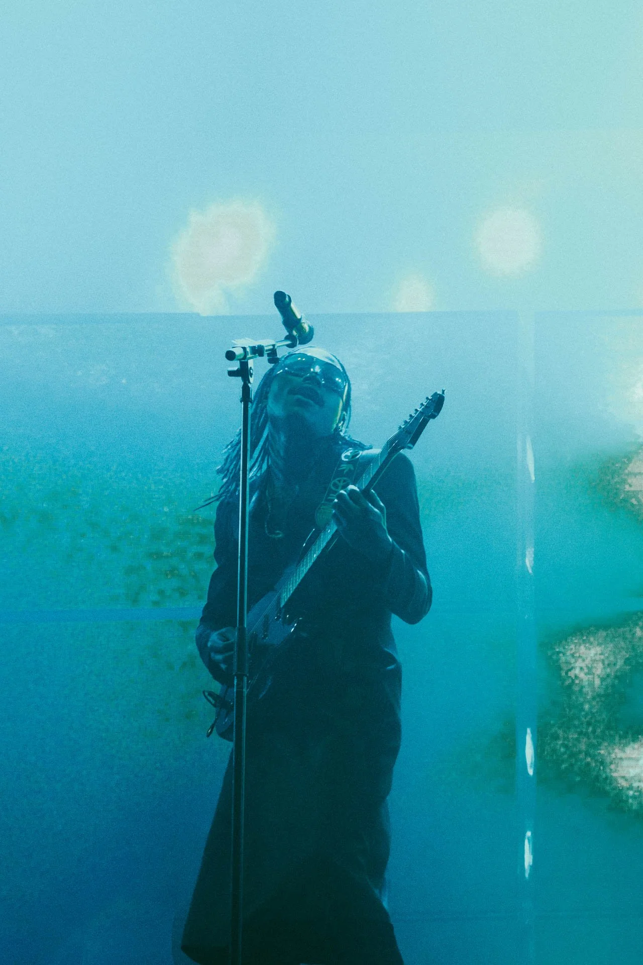 Un musicien joue de la guitare électrique lors d'une performance, avec une audience floue en arrière-plan et une atmosphère sombre