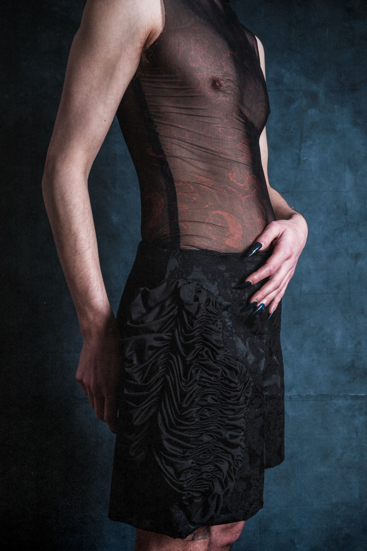 Une femme portant une robe noire en tissu transparent avec des détails floraux en relief, contre un fond sombre.