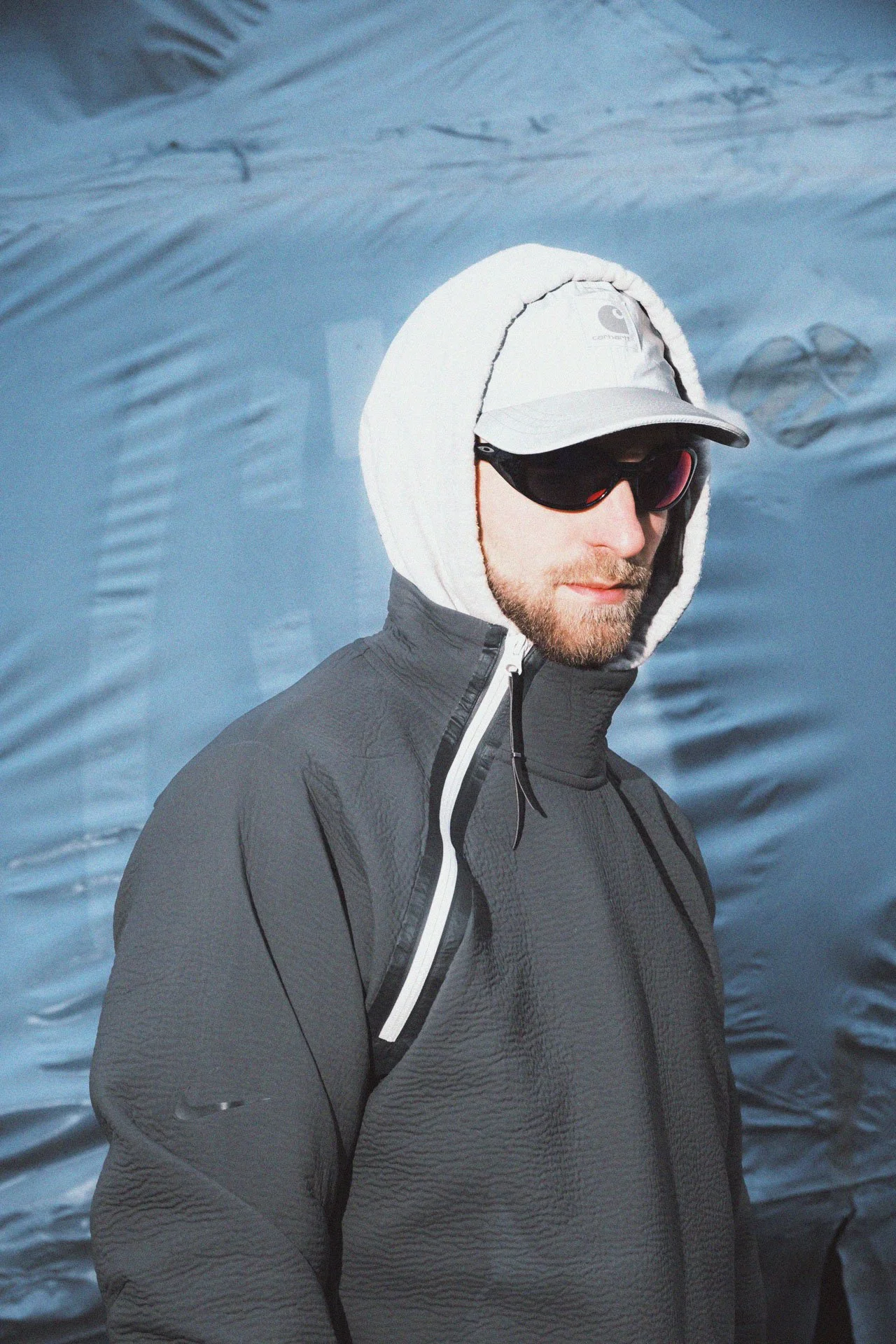 Homme portant une veste noire, un chapeau blanc avec visière, des lunettes de soleil noires, et un hood en fire d'eau.