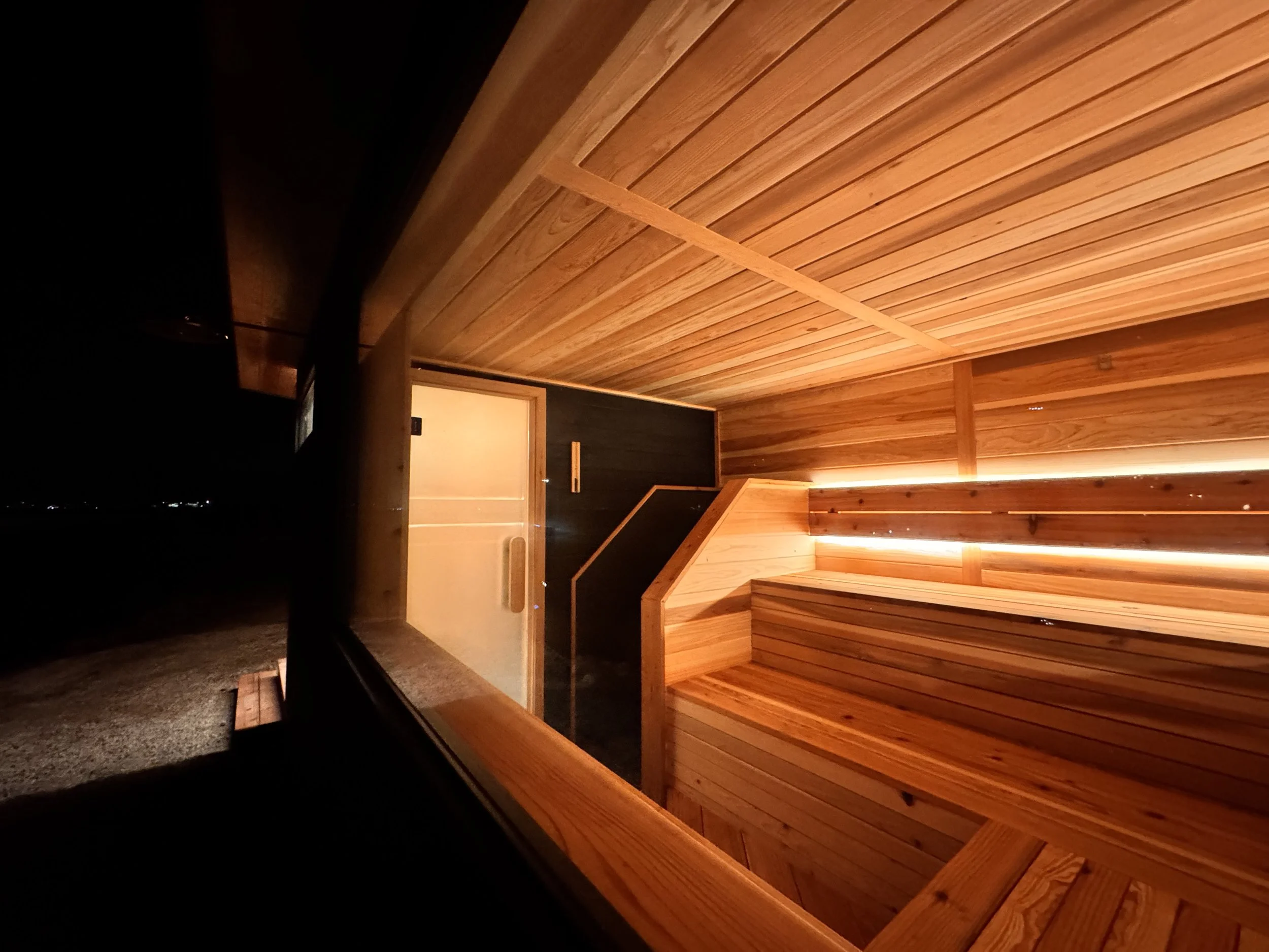 Interior of a sauna with wooden benches, walls, and ceiling, illuminated by warm lighting.