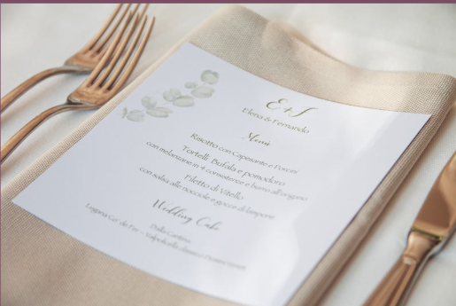 Wedding menu on a paper placed on a beige napkin with gold cutlery on each side.