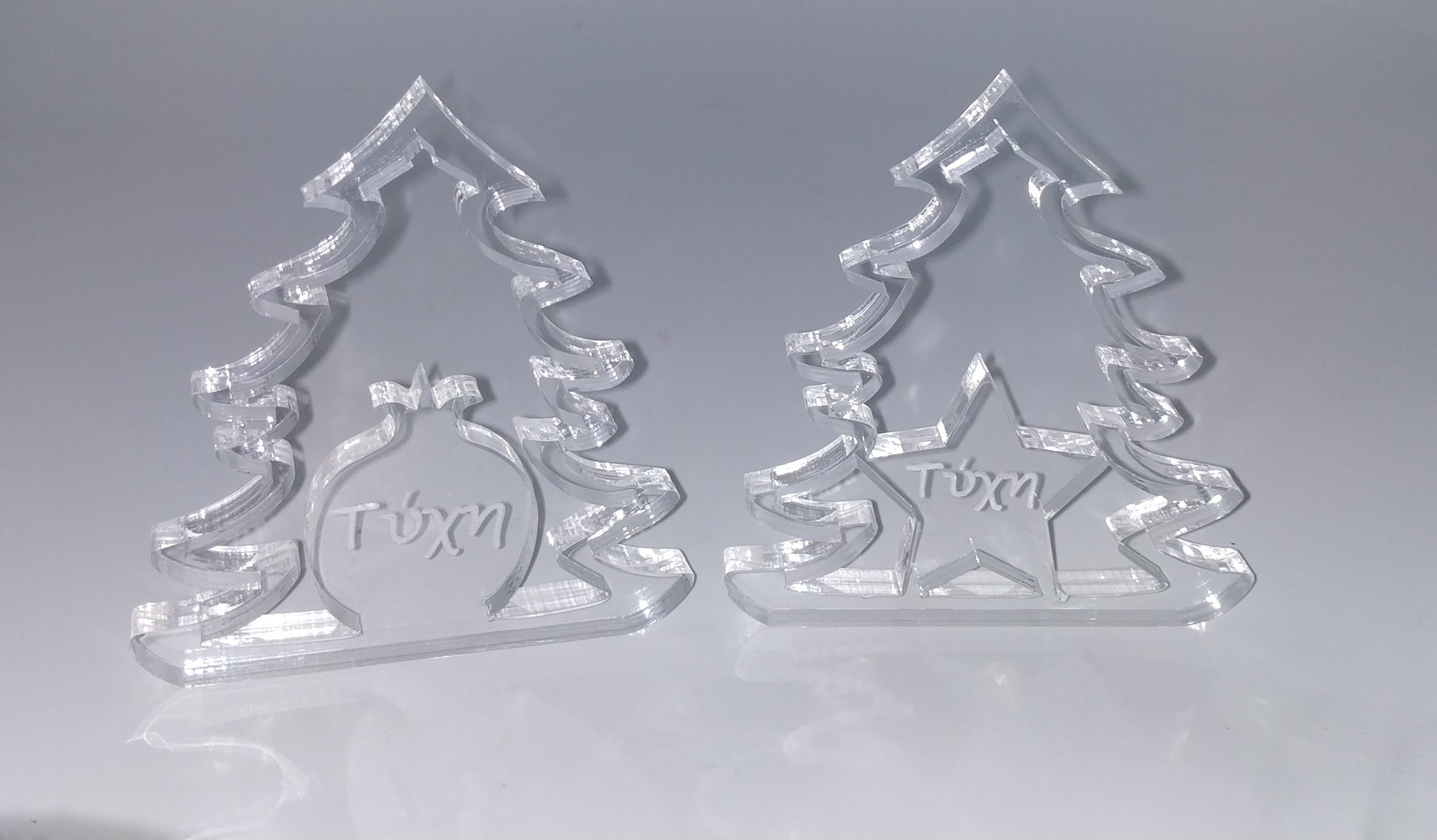 Two clear acrylic Christmas tree decorations with the word "Tuxm" inside a circle on the left and a star with the word "Tuxm" inside on the right.