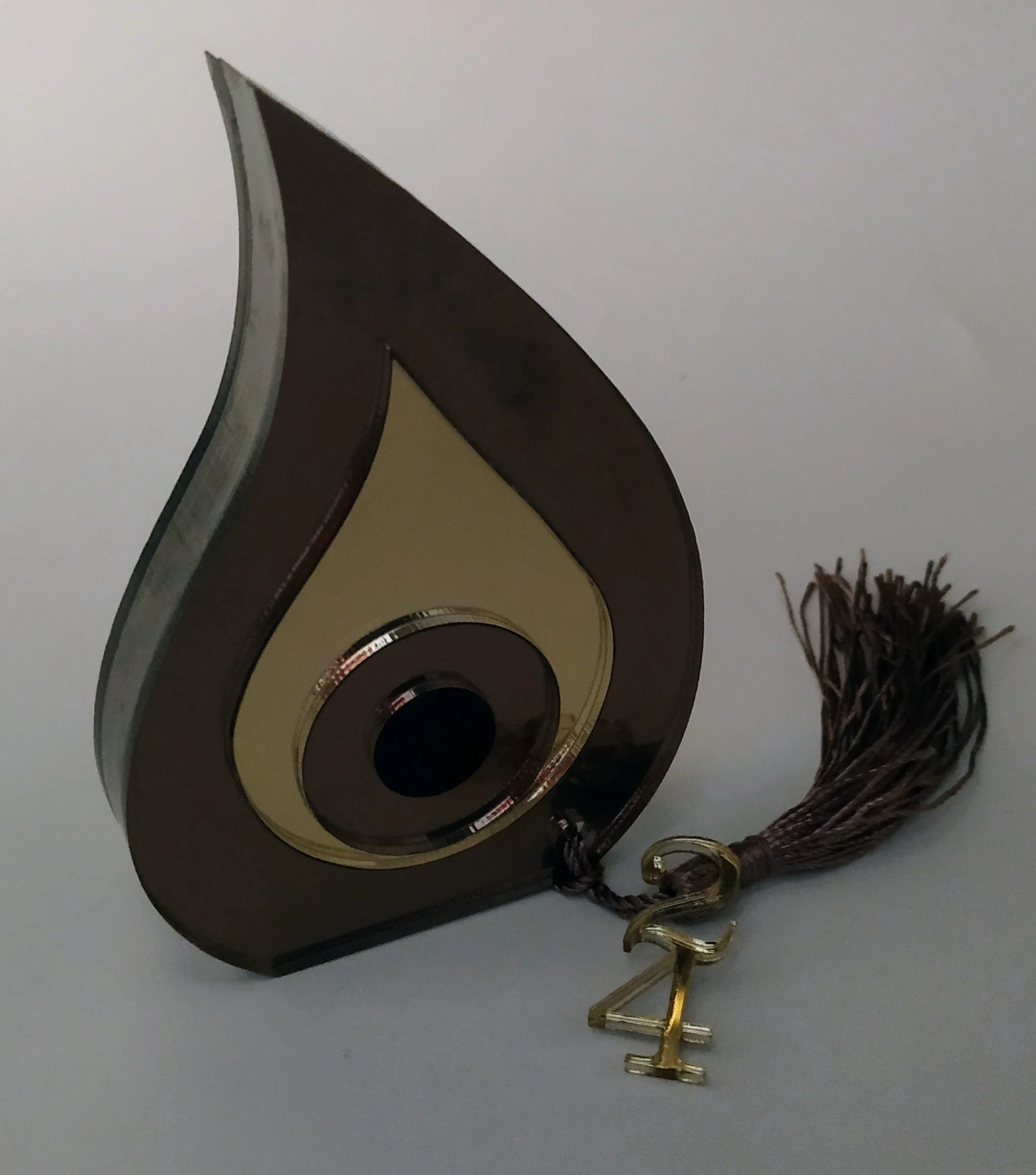 A decorative award plaque with a teardrop shape, featuring a gold and black circular design in the center, attached to a brown tassel with a gold number 24 charm.