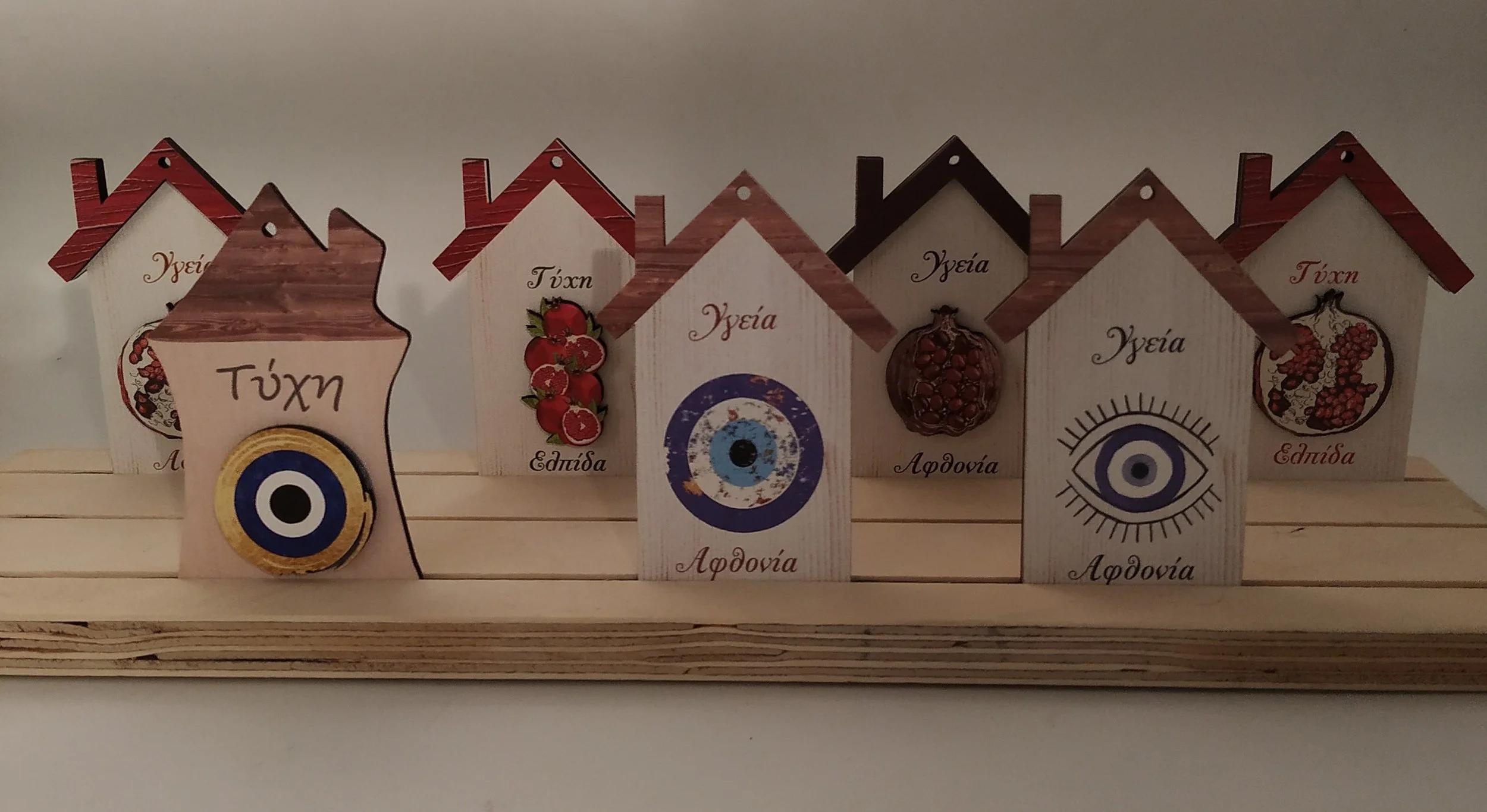 Decorative wooden houses with Greek words and symbols, arranged on a wooden base.