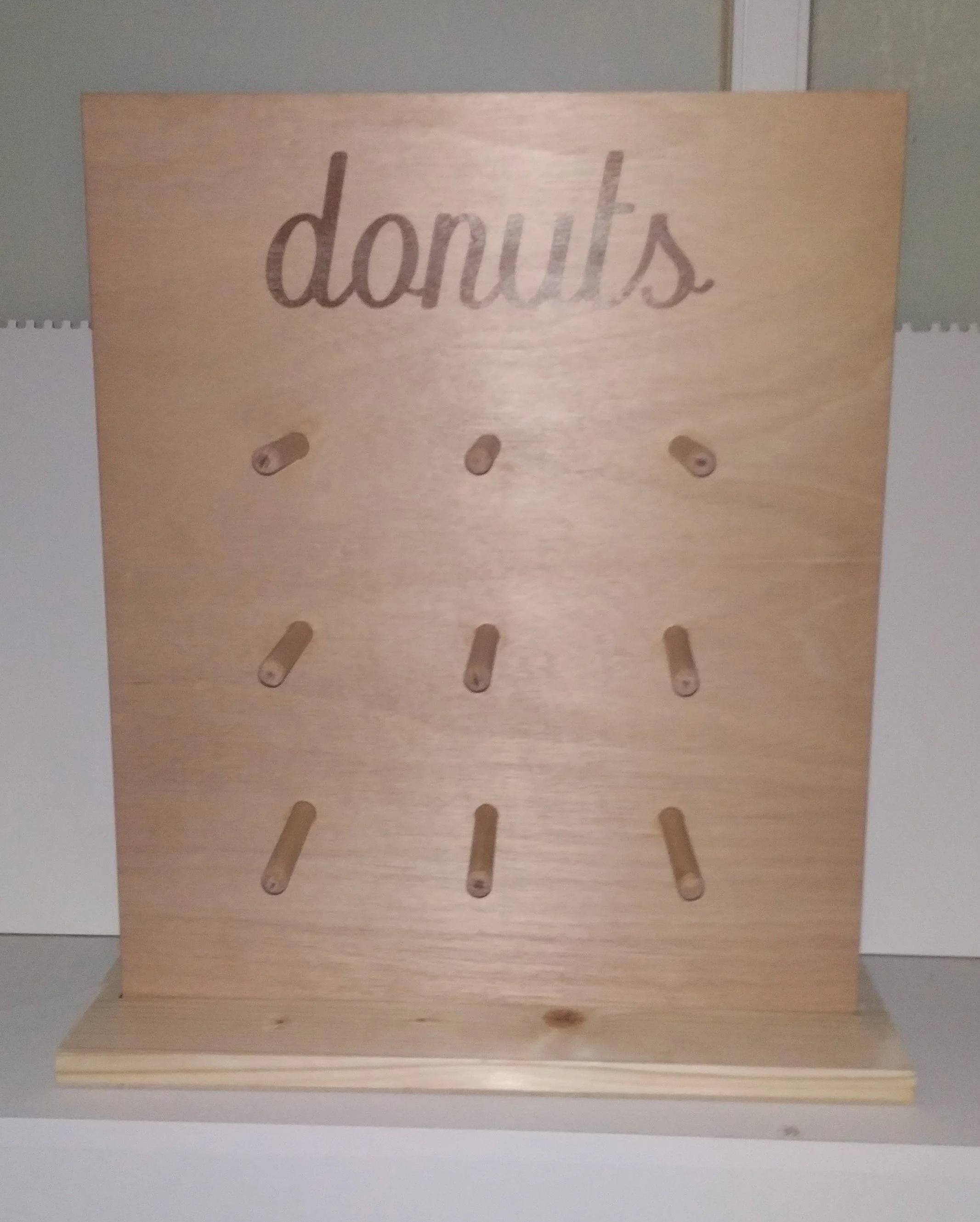 Wooden display stand with the word 'donuts' engraved at the top and multiple horizontal pegs for hanging donuts.