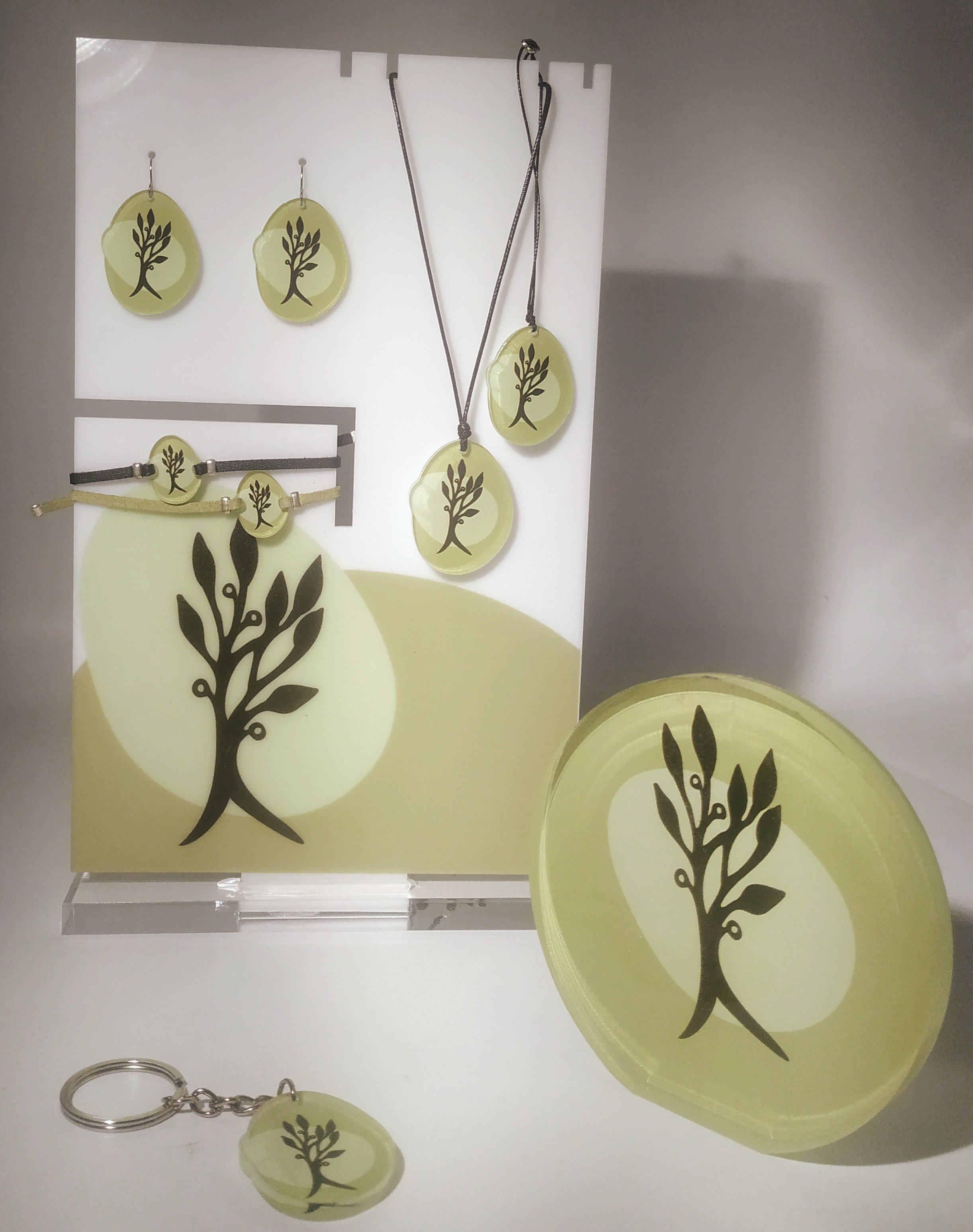 Set of jewelry and accessories with a black tree design on lime green backgrounds, including earrings, necklaces, bracelets, a keychain, and a soap or coaster piece, displayed on a stand.