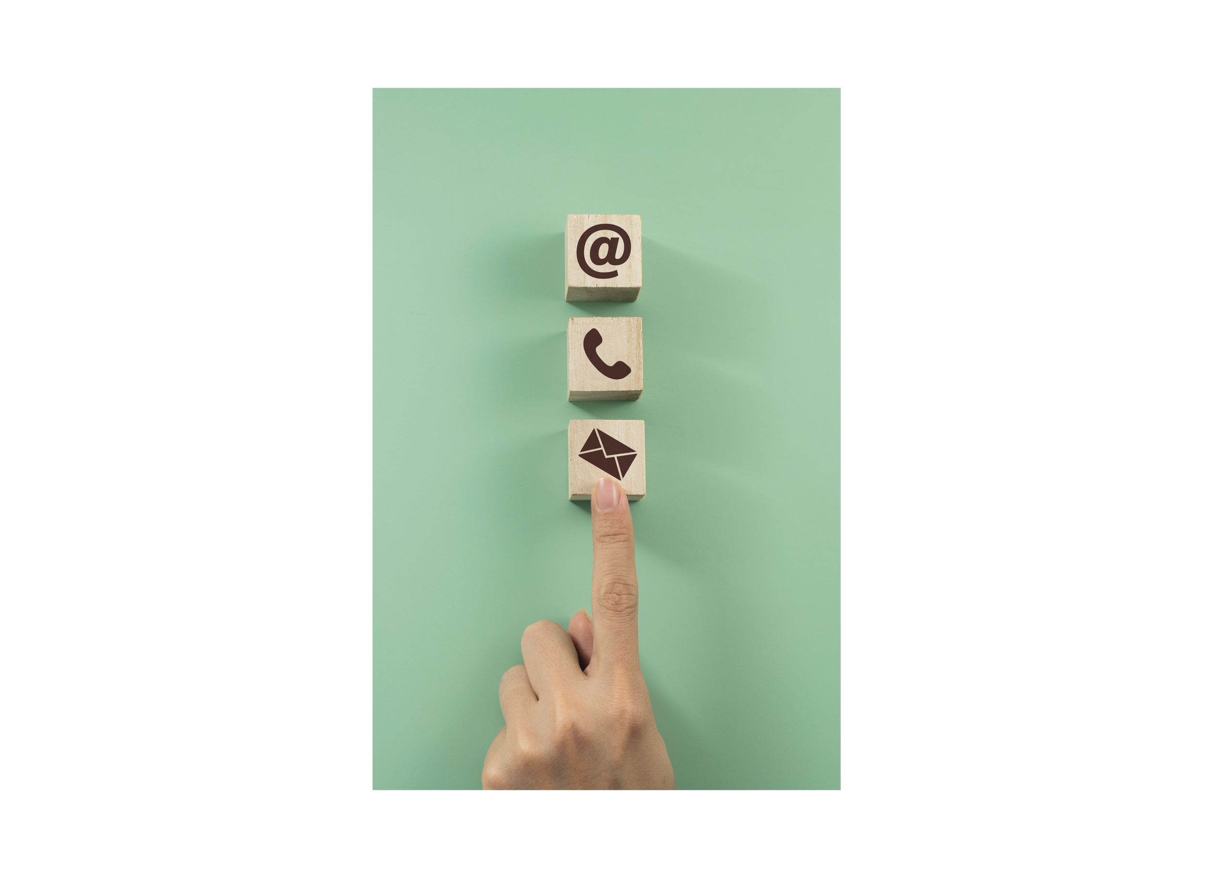 A person's hand with a finger pointing to a wooden block with an email icon on it, surrounded by other blocks with social media and messaging icons on a light green background.