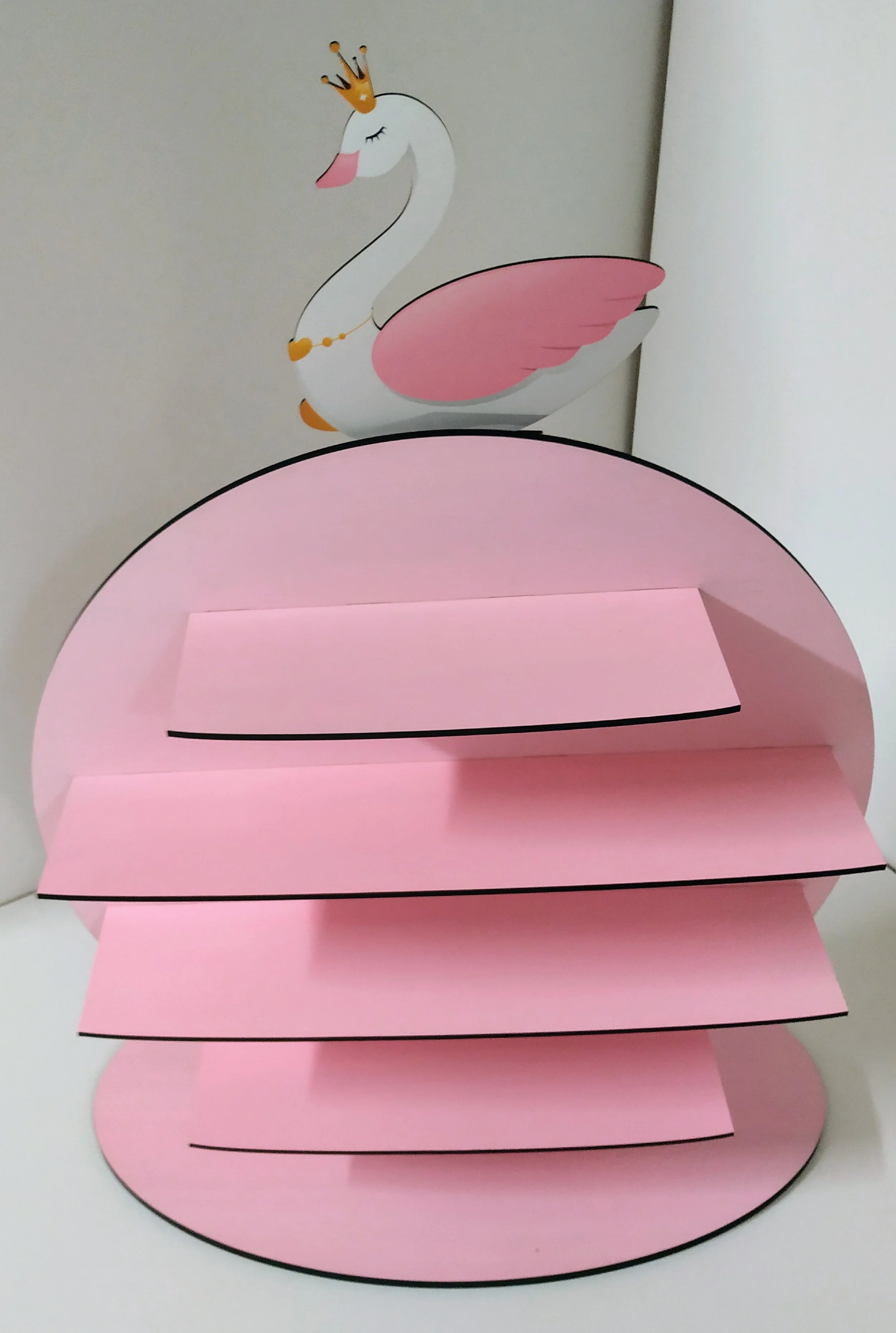 Pink cardboard display stand with multiple shelves and a swan decoration on top, wearing a gold crown and necklace.