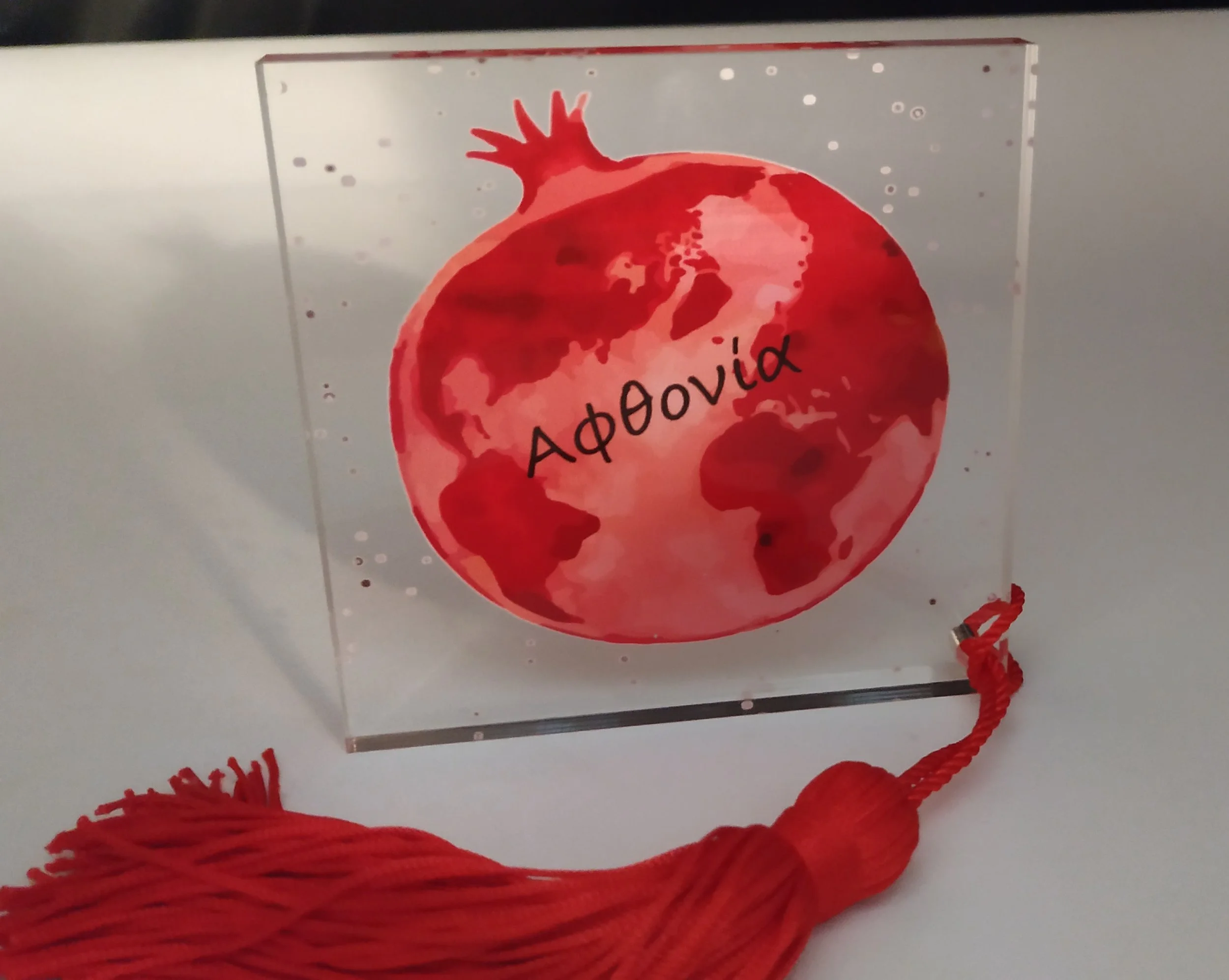A glass award with a red, watercolor-style globe and the word "Αφόβια" written across it, with a red tassel attached at the bottom.
