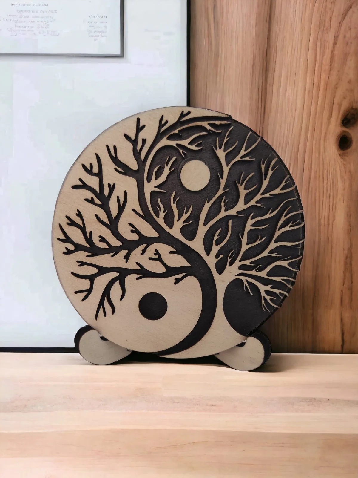 Decorative wooden circle with cut-out design of a tree and yin-yang symbol, placed on a wooden surface in front of a framed document.