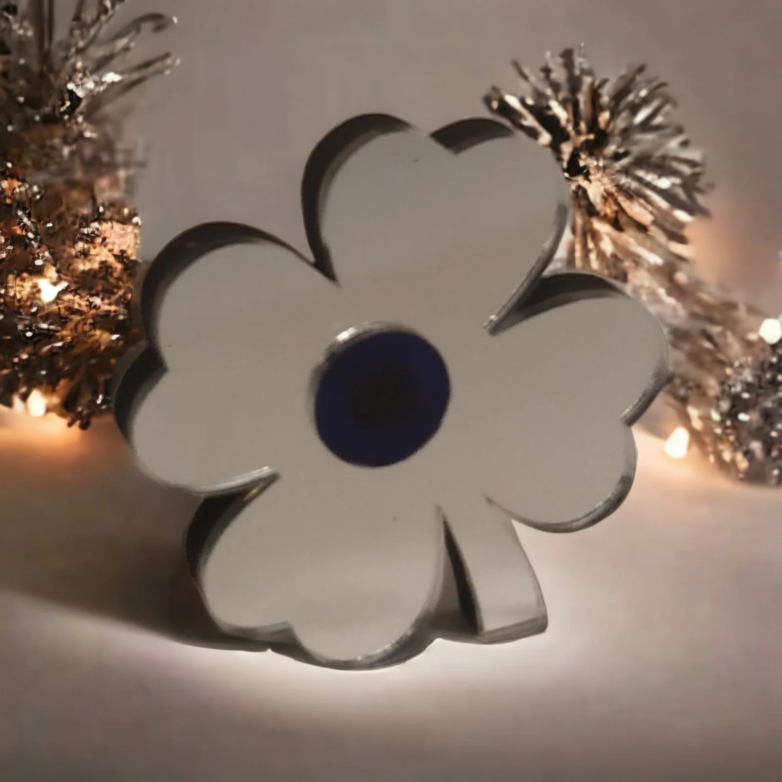 A metal cookie cutter in the shape of a flower, placed on a surface with gold-colored tinsel and small lights in the background.