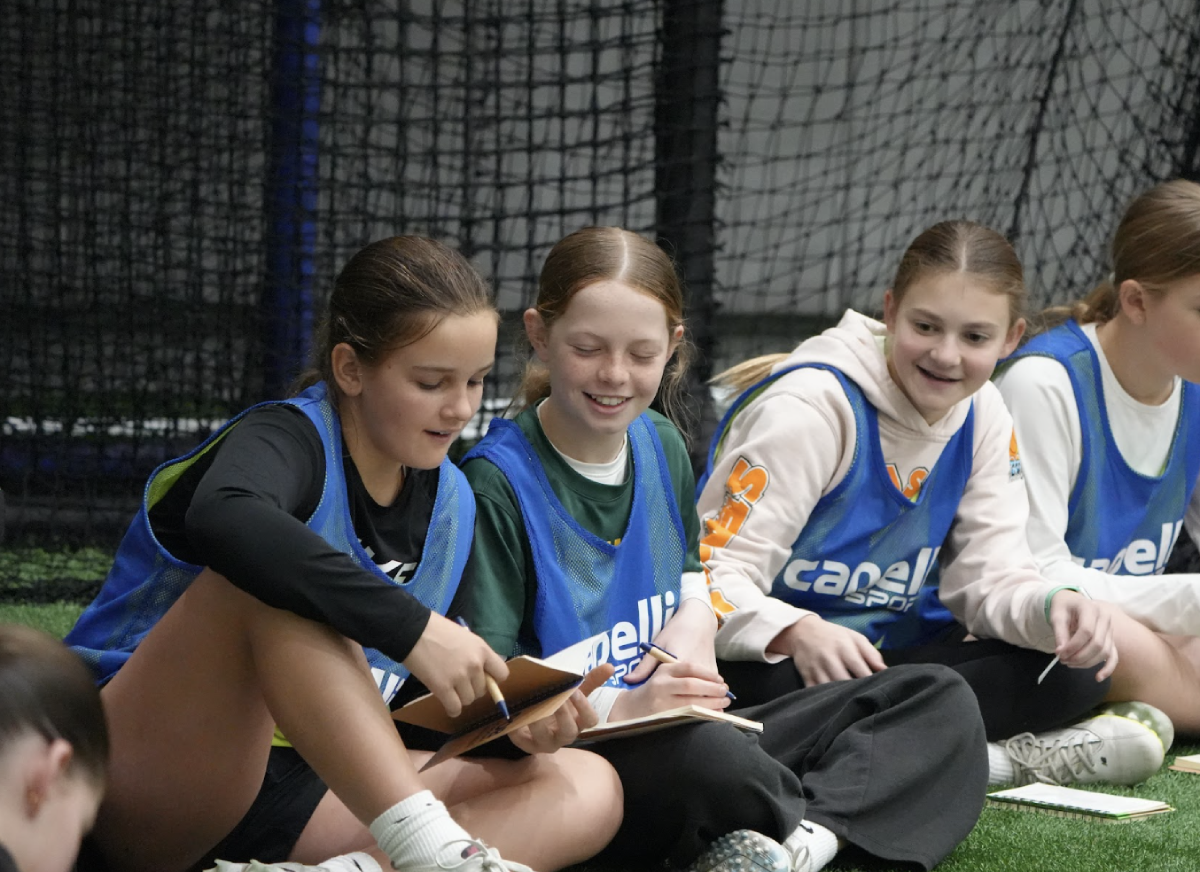Young girls lacrosse players smiling and sitting together in pinnies during a Tenacity Sixes Academy mini-camp event