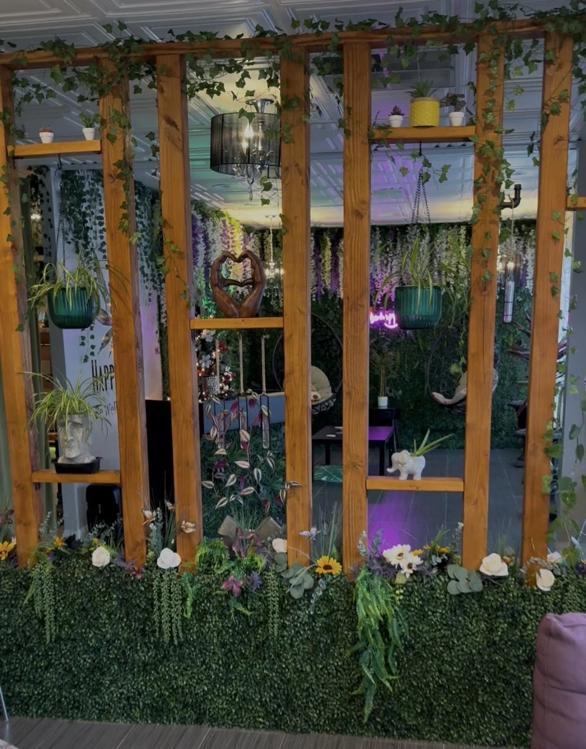 Decorative indoor space with hanging and potted plants, a wooden lattice divider, and colorful lighting.