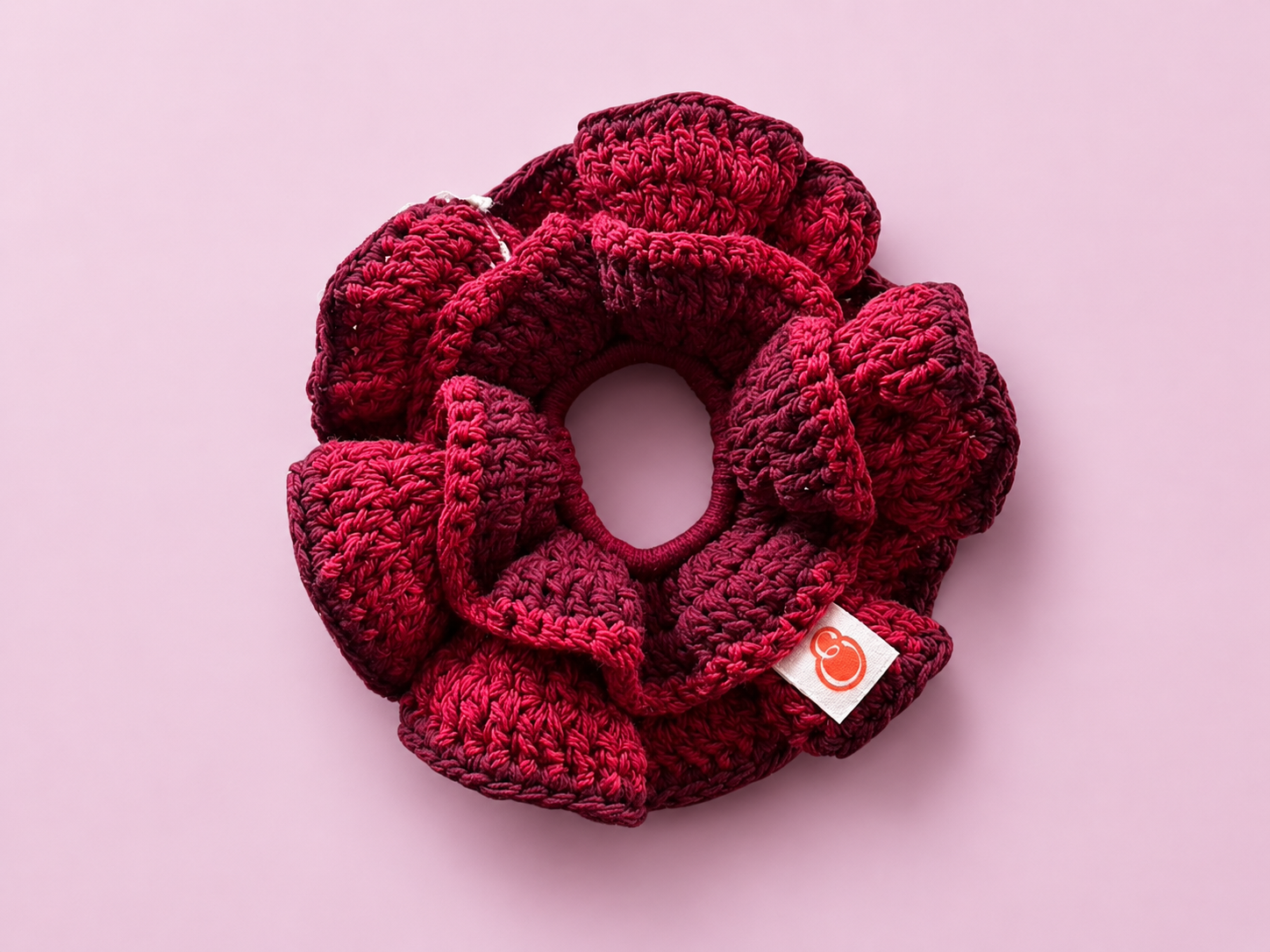 A red knitted scrunchie with a fabric tag on a light pink background.