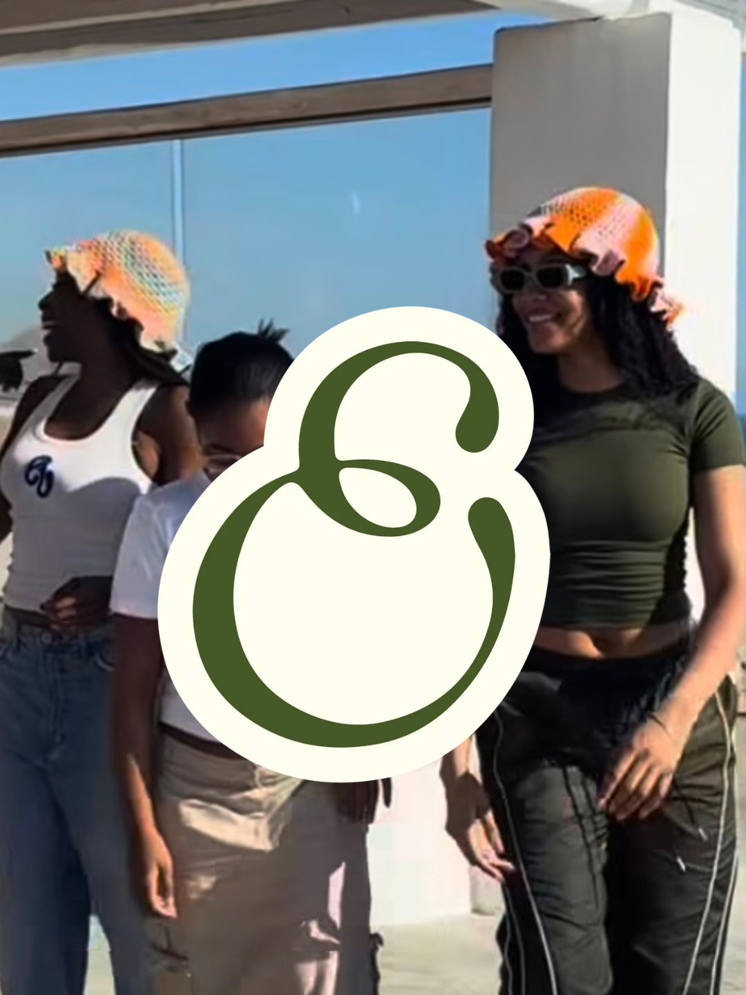 Group of people outdoors wearing colorful knit hats, standing near a glass building, with a large white sticker covering part of the image.