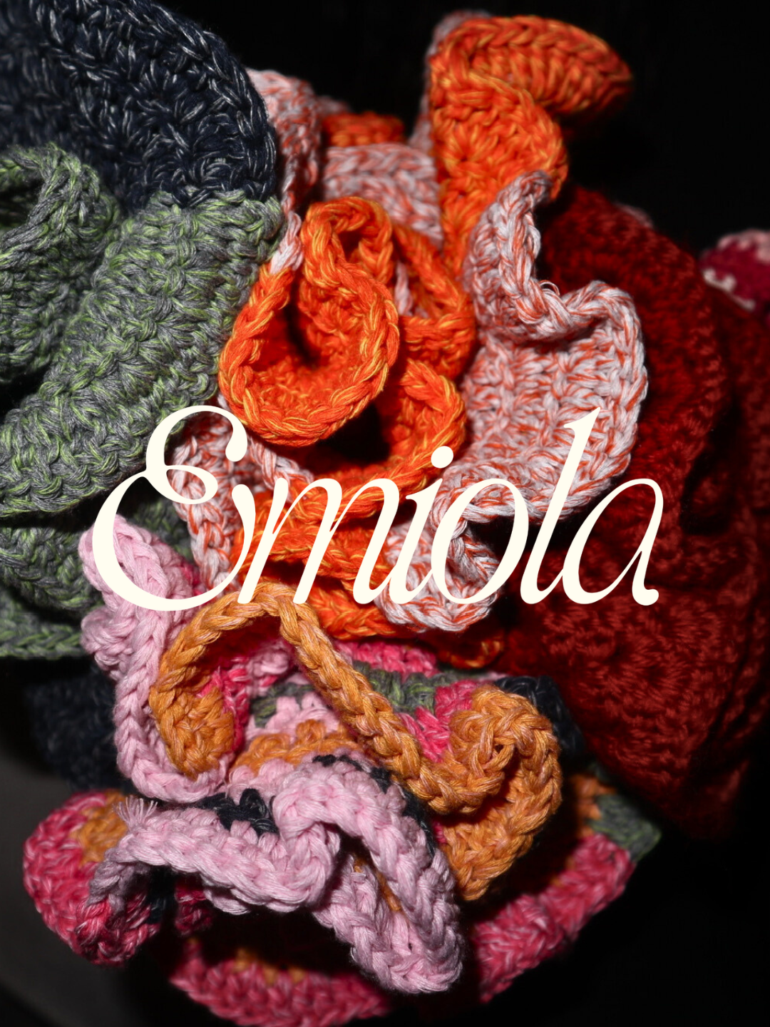 A collection of colorful crocheted fabric hair scrunchies with the logo 'Emiola' written in white cursive across the image.
