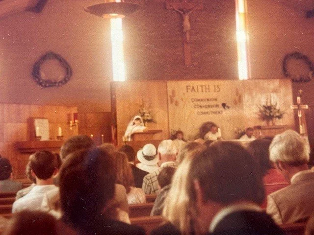 Indoor church service with congregation facing altar, wooden cross, and a banner reading 'FAITH IS' with words 'more than' faintly visible.
