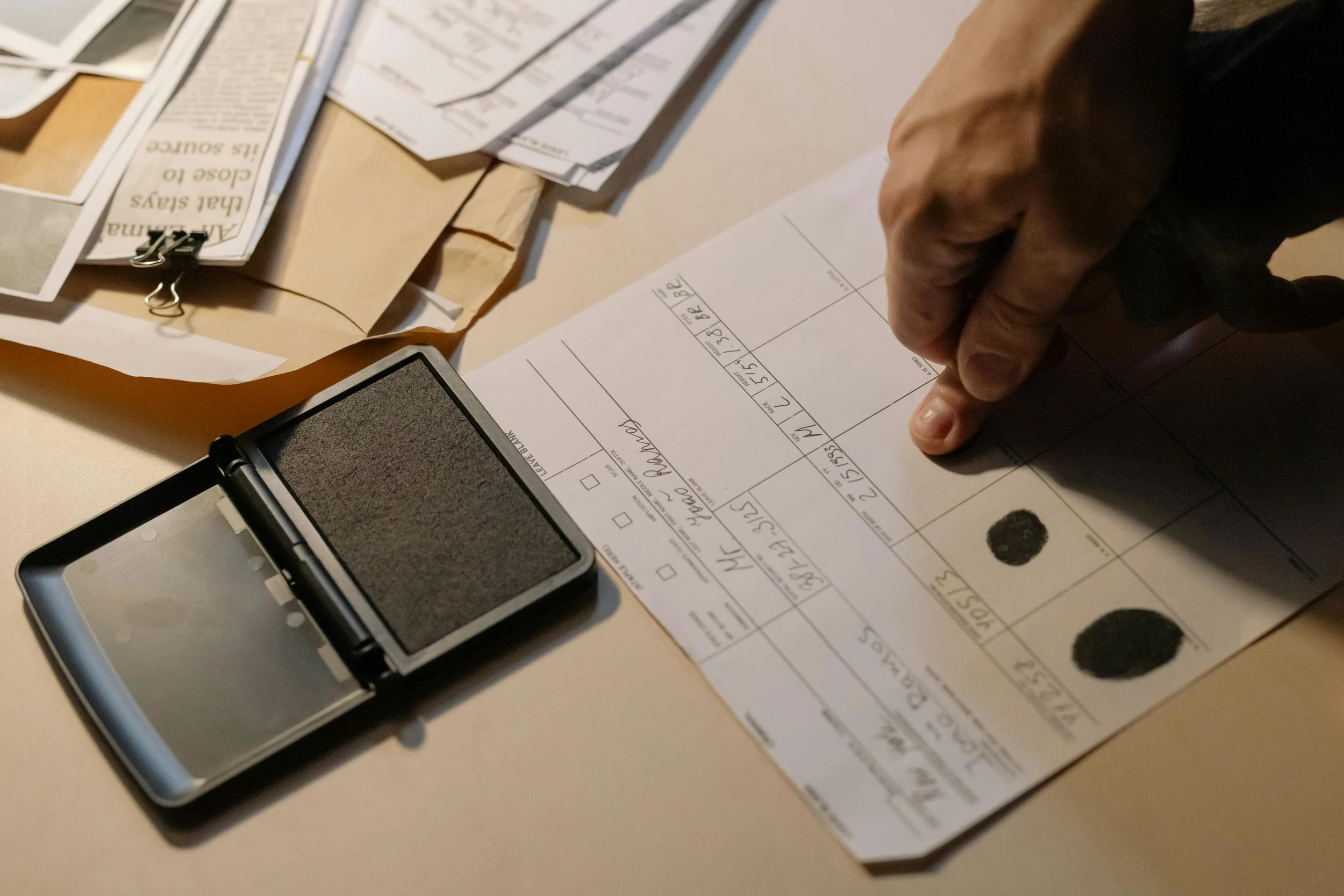 A hand stamping a ballot paper at a voting station with documents and a black ink stamp nearby.