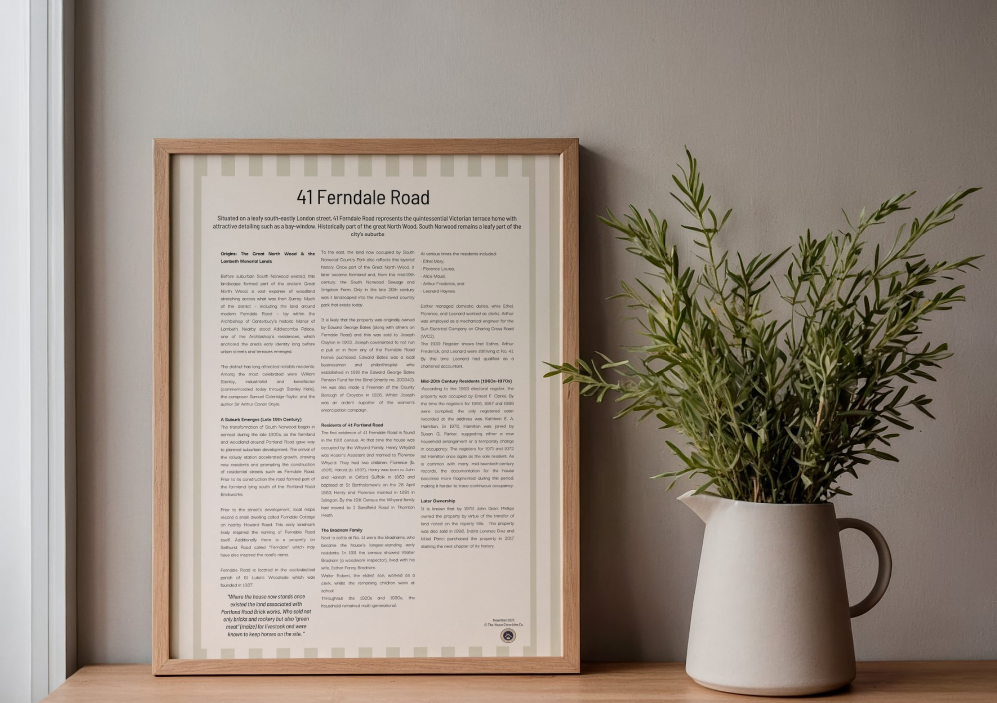 A framed informational poster titled '41 Ferndale Road' next to a potted leafy green plant on a wooden surface, with a gray wall background.
