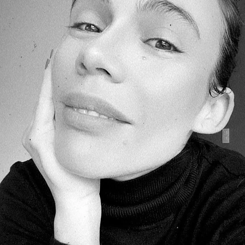 Close-up black and white photo of a person resting their face on their hand, with short hair, wearing a dark turtleneck sweater.