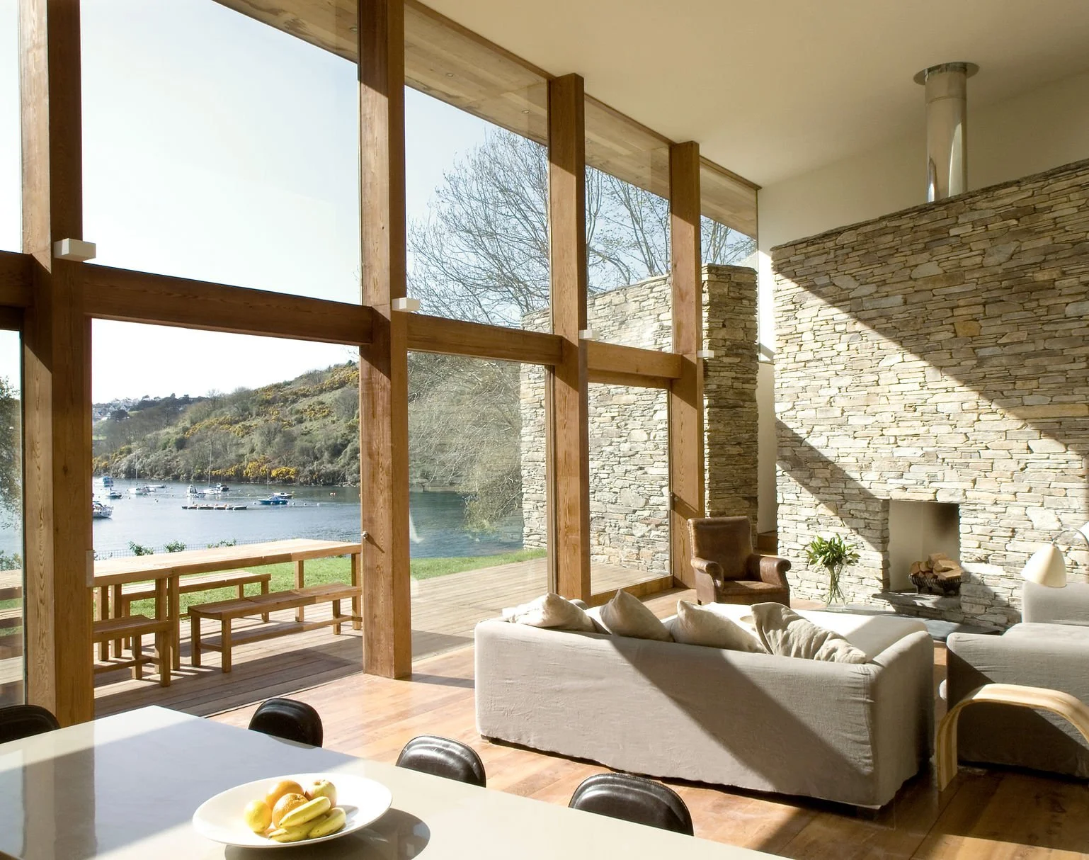 Luxury living room with panoramic river views, floor-to-ceiling windows, natural wood accents, and stone fireplace