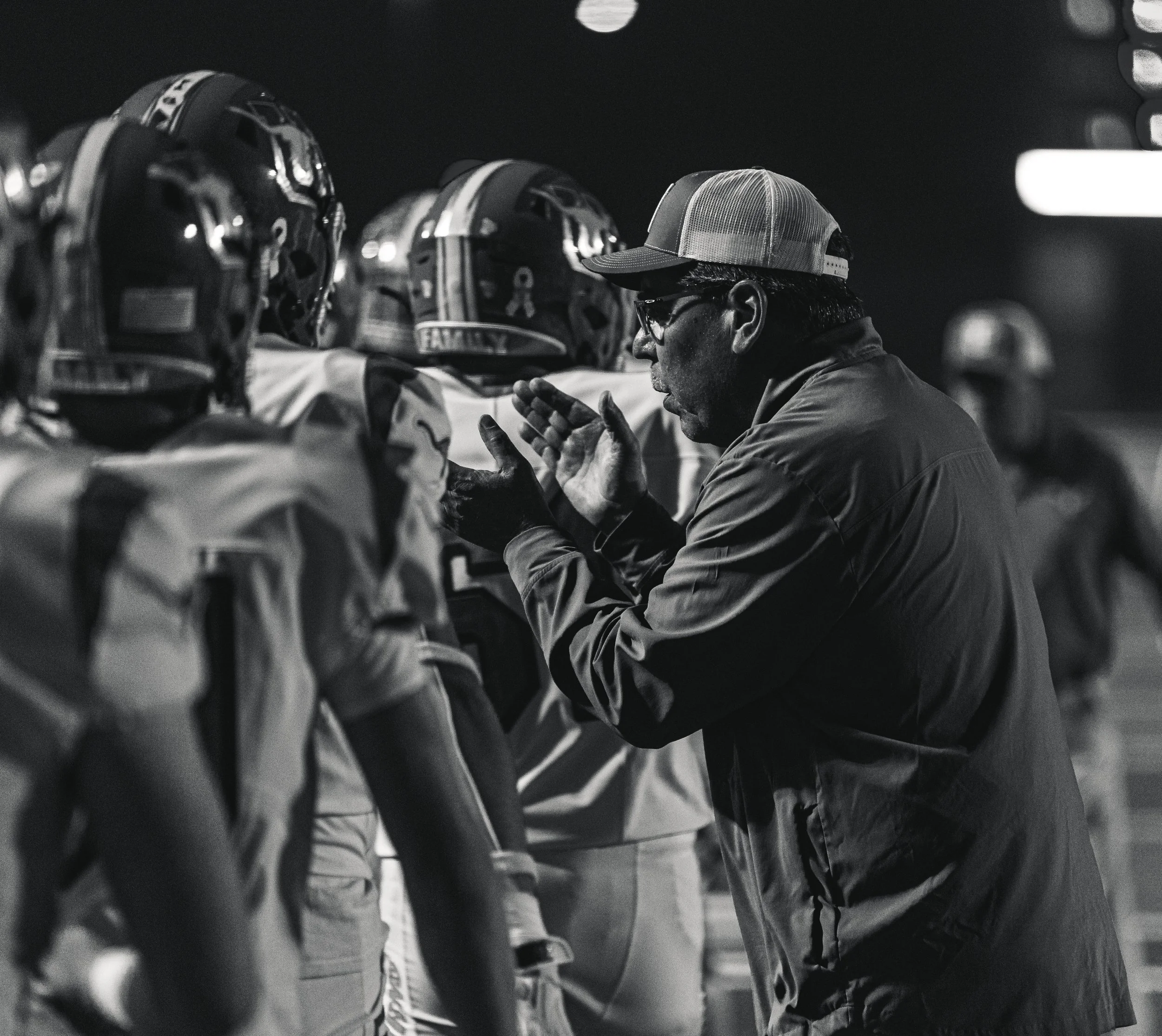 A coach giving instructions to football players during a night game.