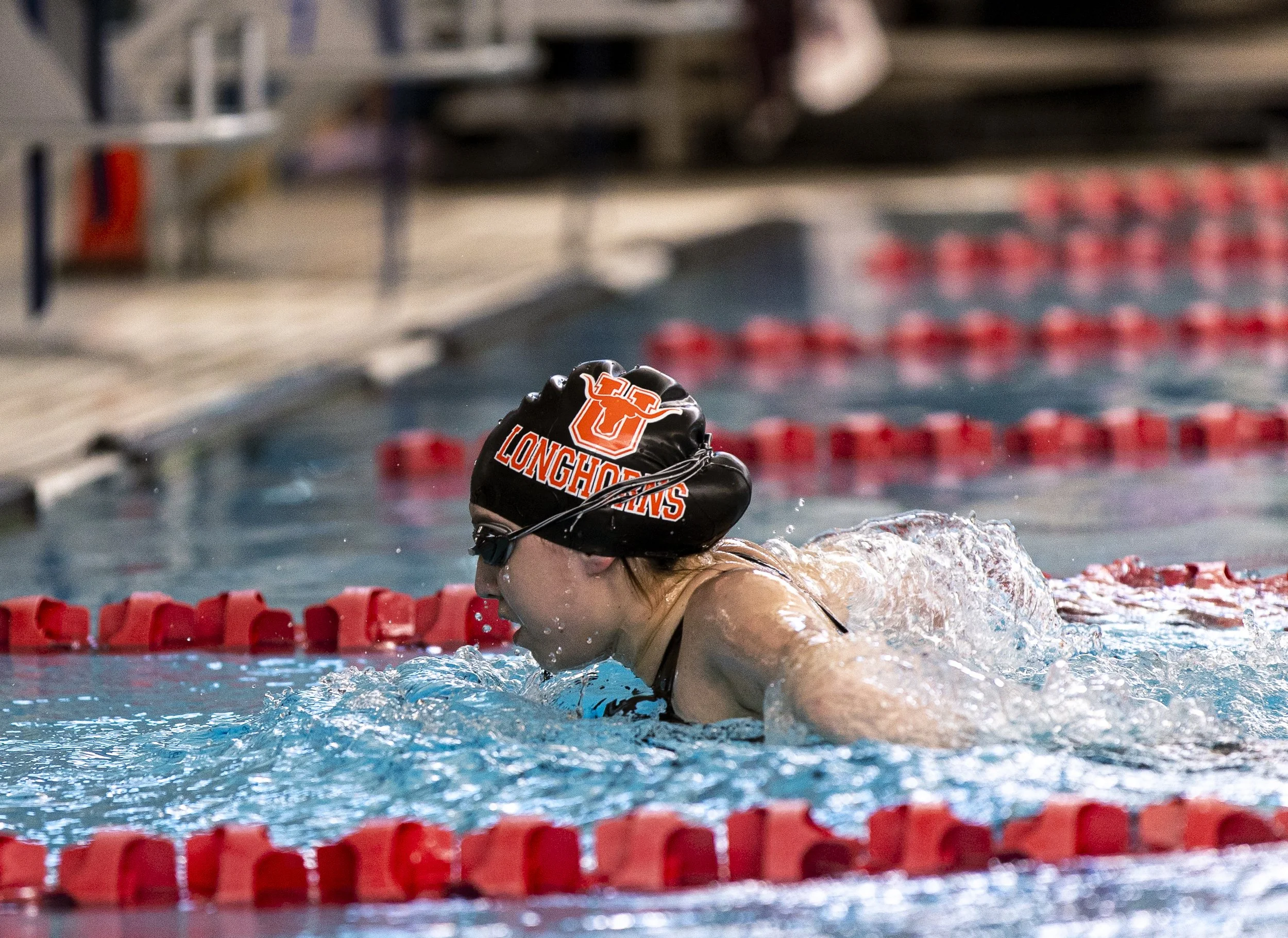 Swimmer wearing a black cap with the Utah Utes logo and 'Longhorns' written on it, performing the butterfly stroke in a swimming pool.