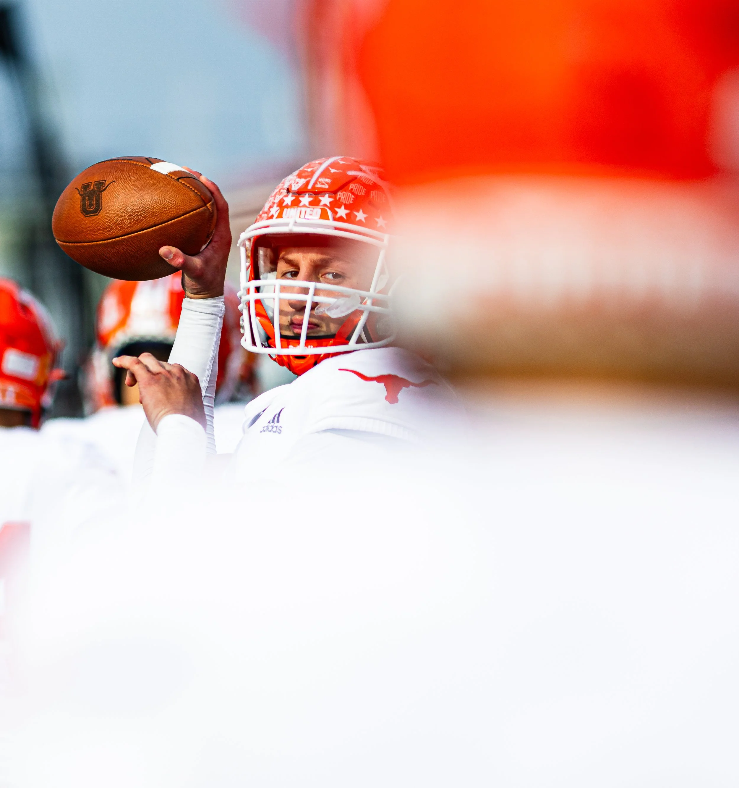 A football player in a white uniform and red helmet holding a football with a focused expression.