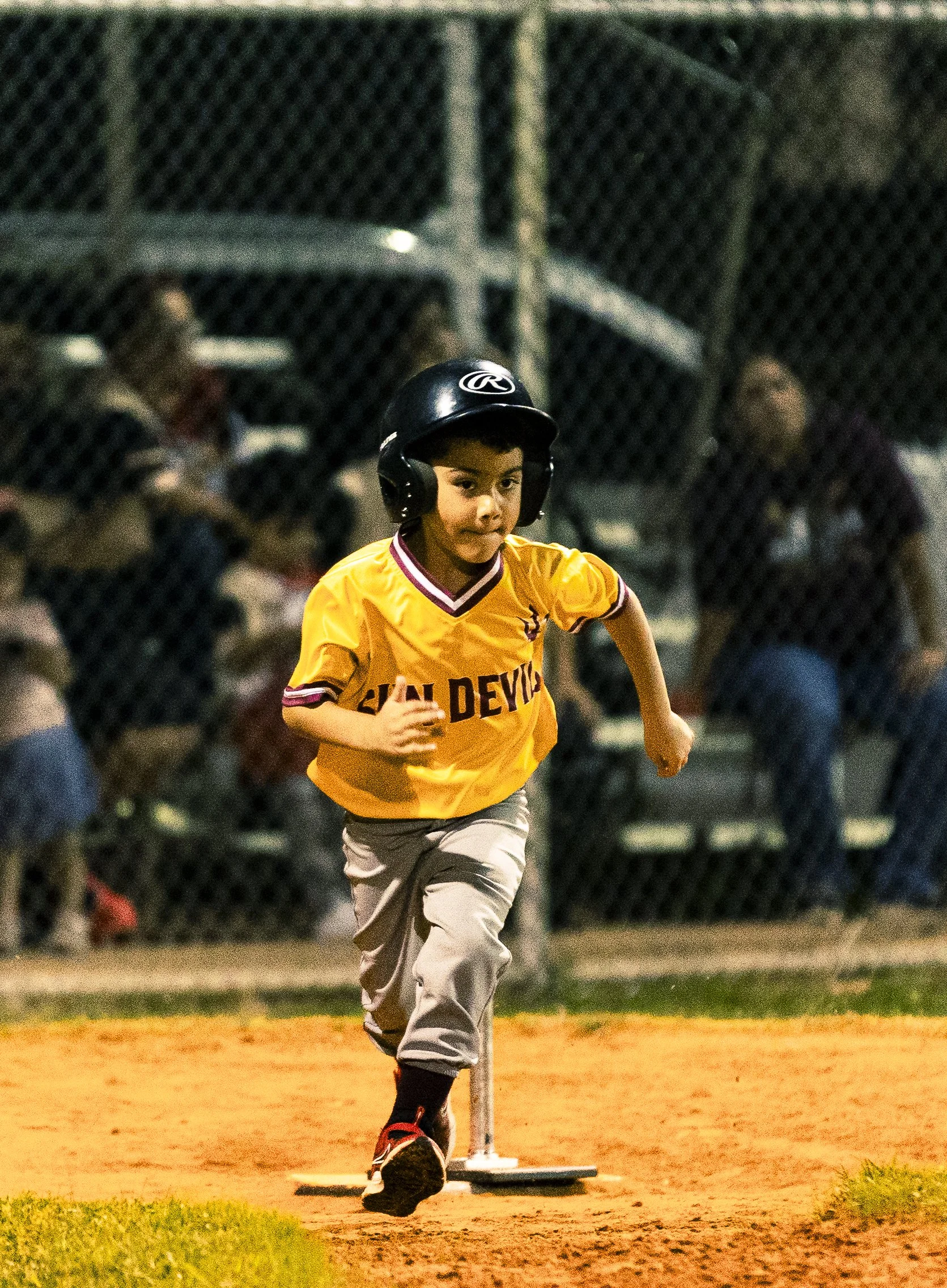 Young baseball player in yellow jersey running at home plate during a game at night.
