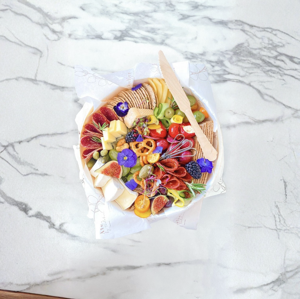 A colorful charcuterie board filled with various cheeses, fruits, crackers, and edible flowers on a white marble surface.