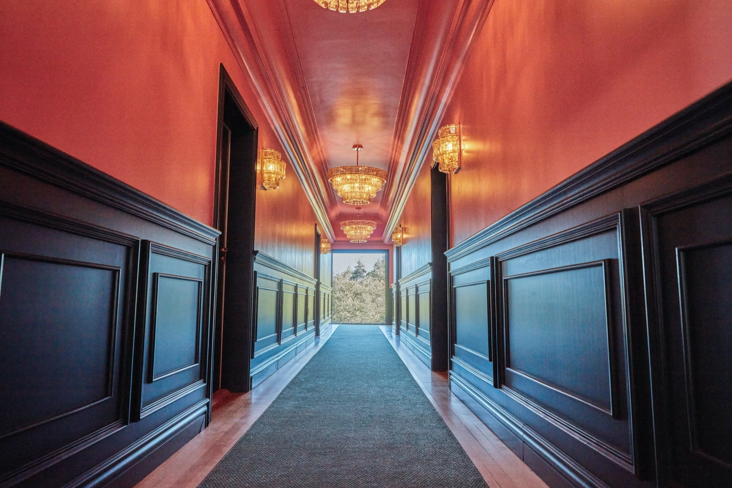 A Lodge hallway with a pink ceiling, dark green paneled walls and brass lights.