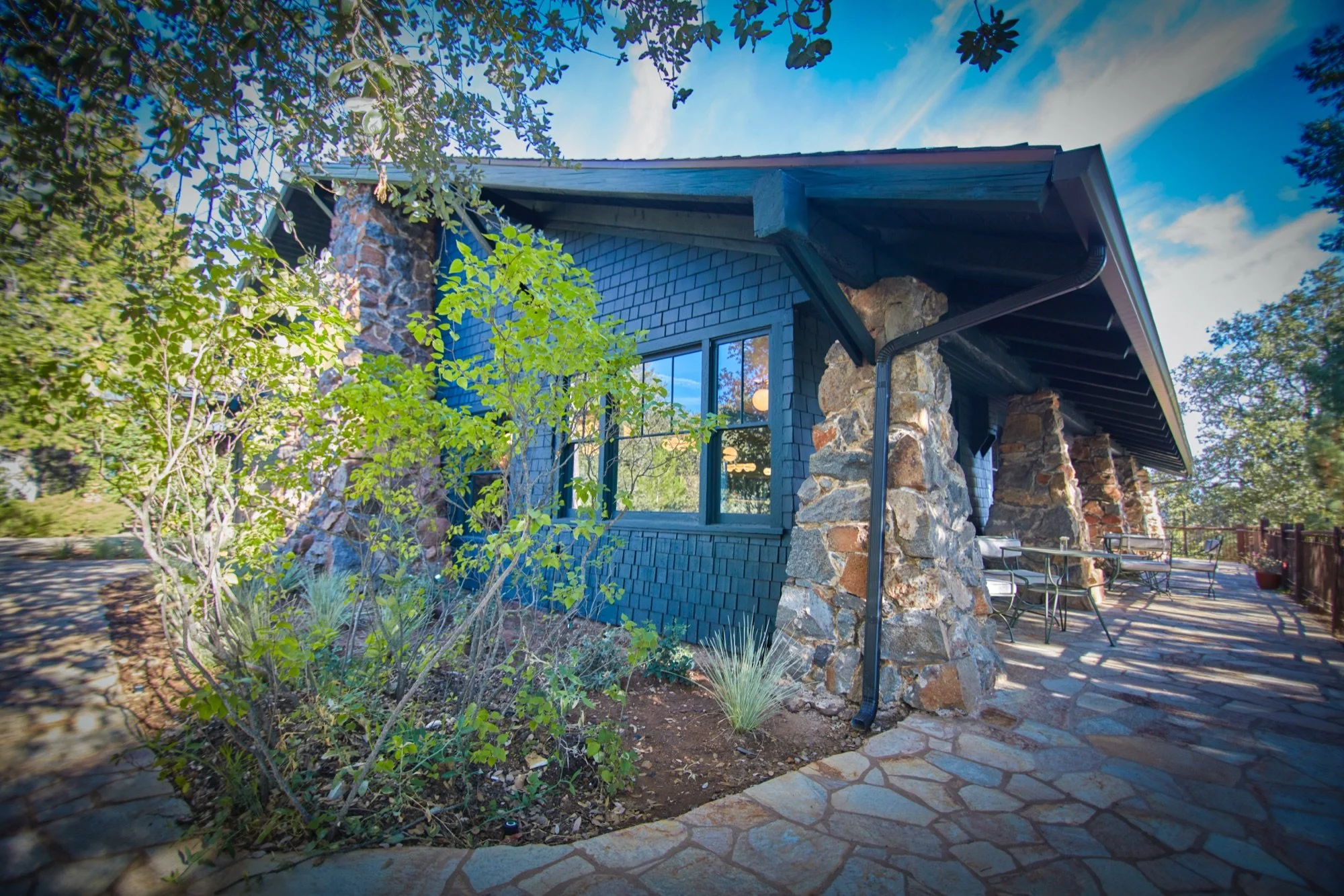 Native stone pillars and a shaded porch beside a flagstone patio.