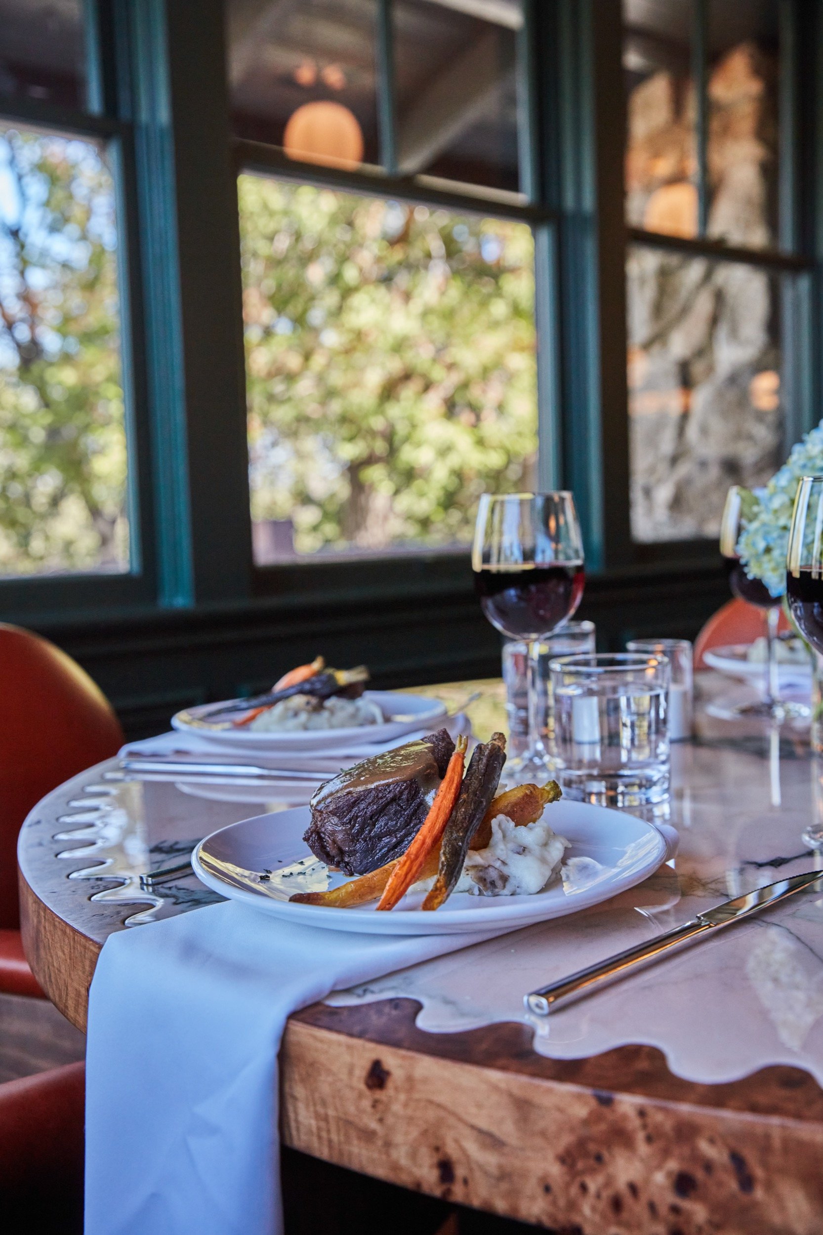 A table set with wine and hydrangeas beside The Lodge's tall windows.