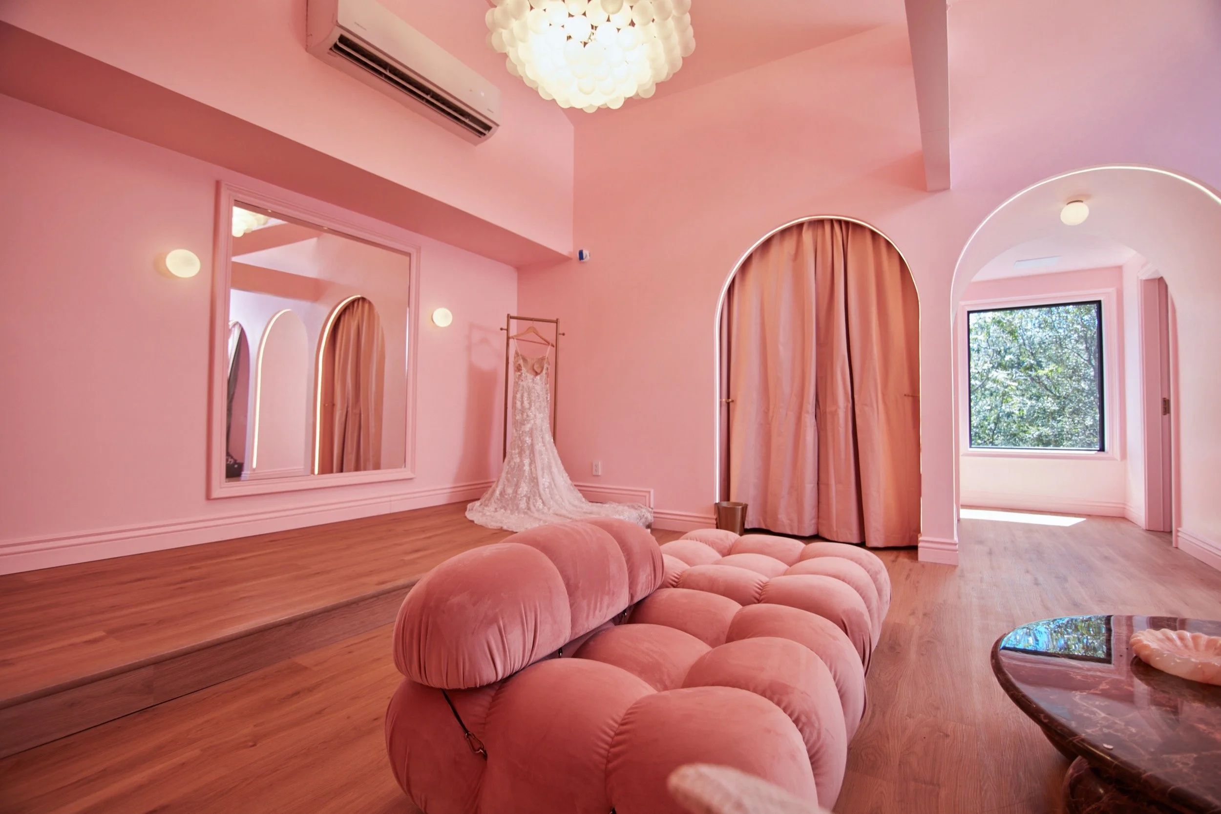 A wedding gown by the mirror in the Bridal Suite, beside a pink tufted sofa.