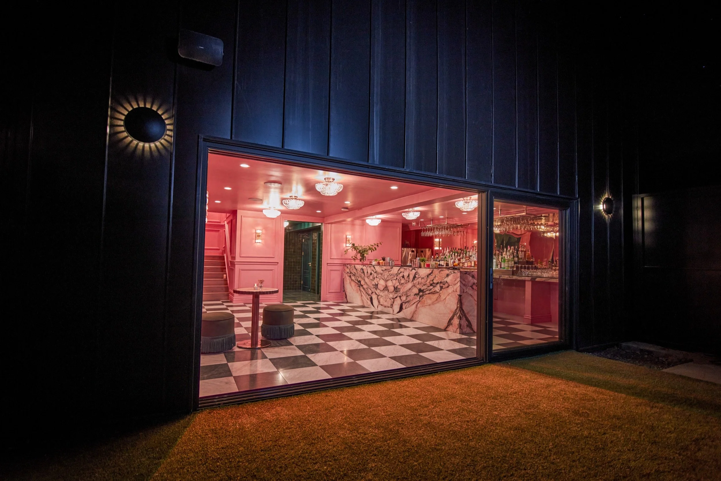 The pink bar glowing through glass doors at night, set into the dark blue exterior.