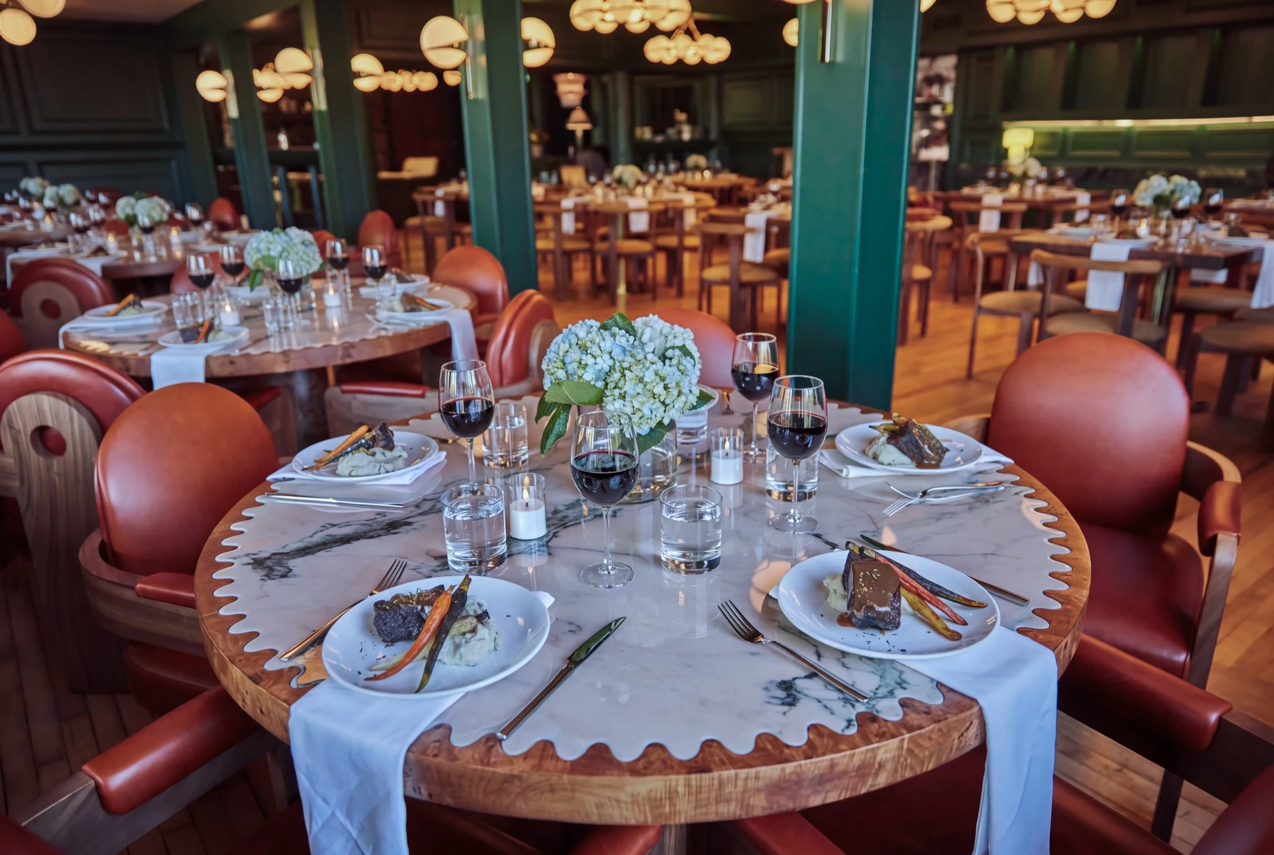 A round table set for dinner with white hydrangeas among green columns.