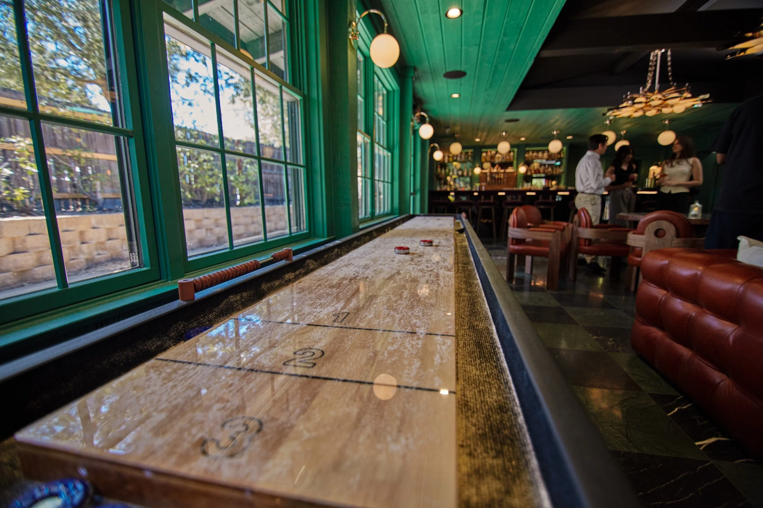 The Lodge Bar, with green walls, a long shuffle board and brass pendant lights.
