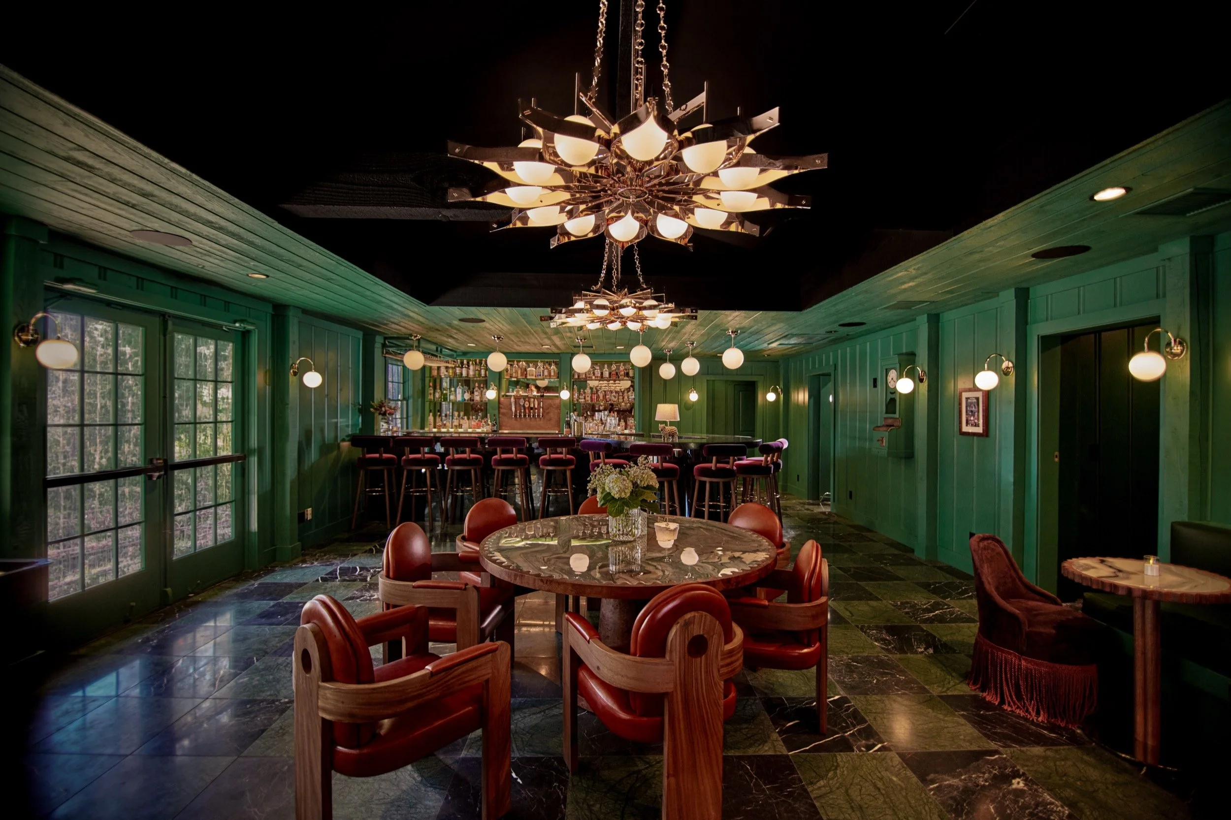 Round tables and leather chairs beneath a starburst chandelier in The Lodge Bar.