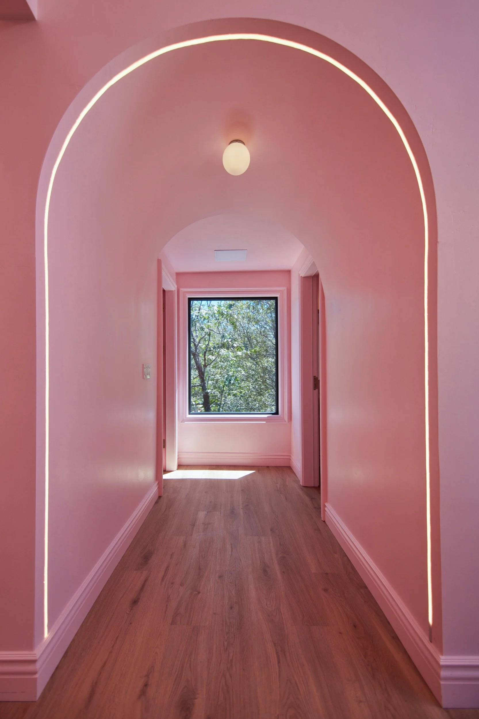 An arched pink hallway in the Bridal Suite leading to a window framed by trees.