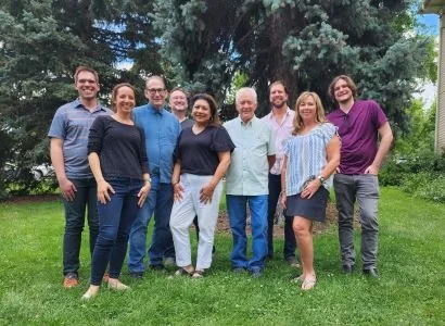 Group of seven people standing on grass in front of trees, smiling for a photo.