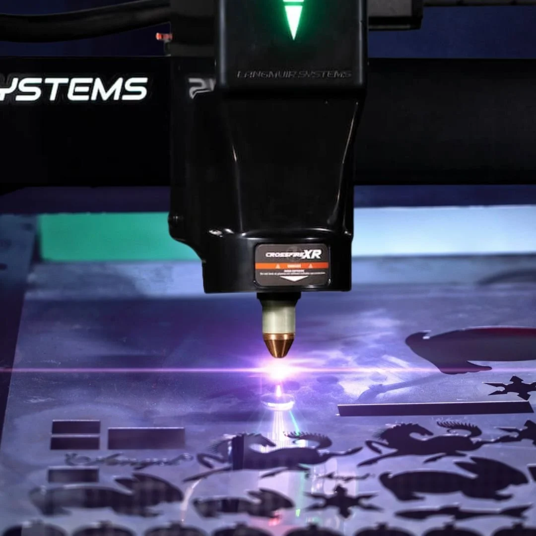 A CNC machine is cutting intricate designs of dragons and other shapes from a sheet of metal in a factory or workshop.