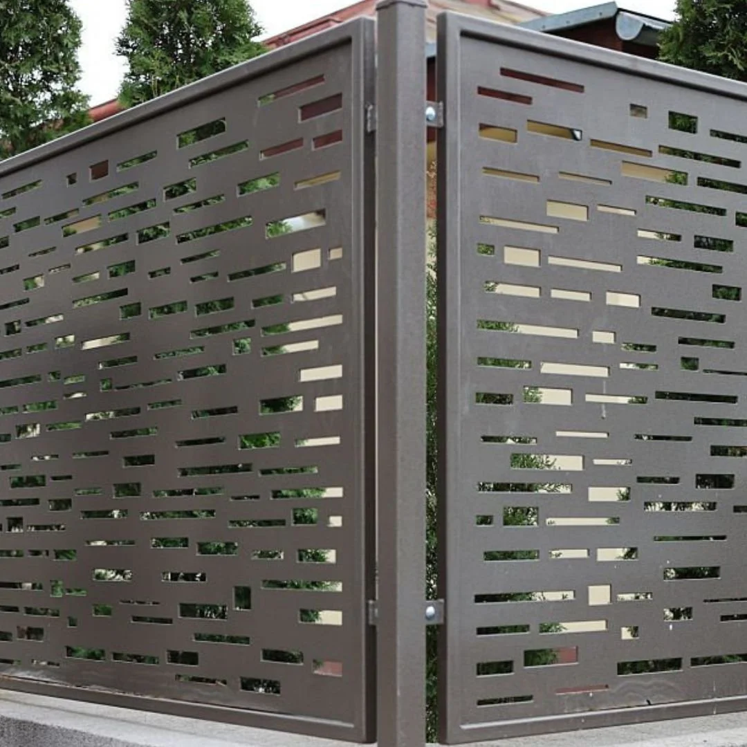 A modern metal fence with rectangular cutouts, partially open, with greenery visible through the gaps.